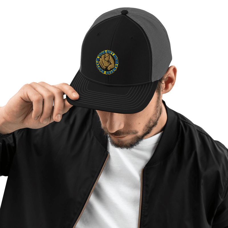 Man wearing a black and grey trucker hat and black jacket, top of his head tilted down