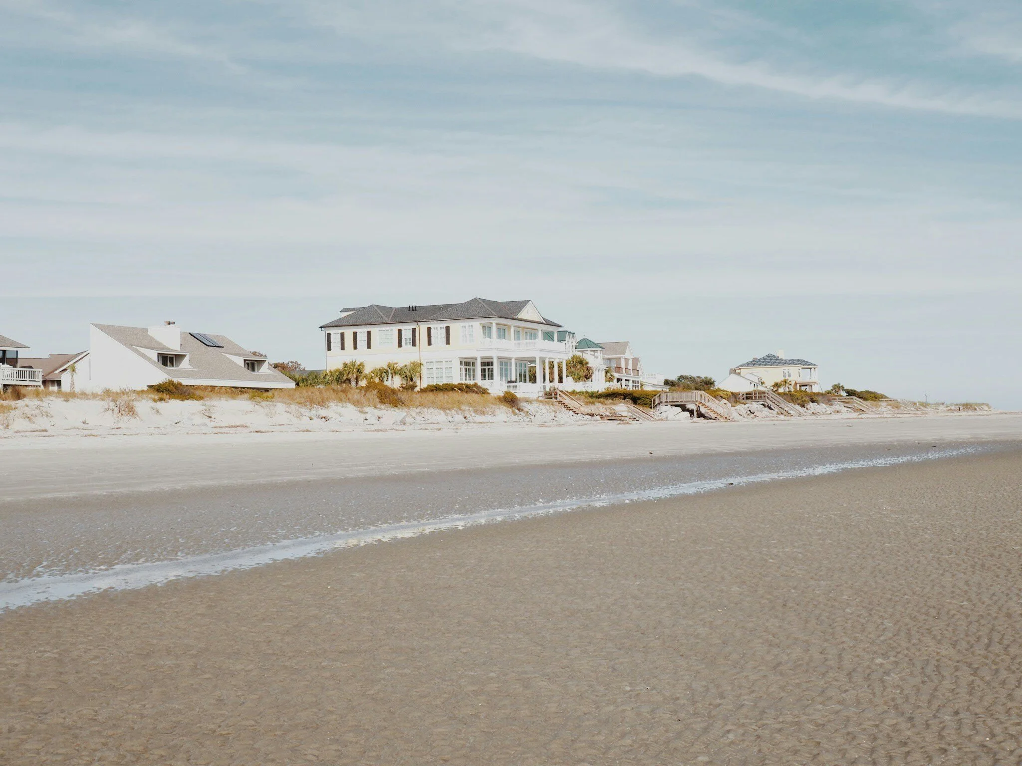 Seaside houses on a sandy beach, with a cloudy sky above.