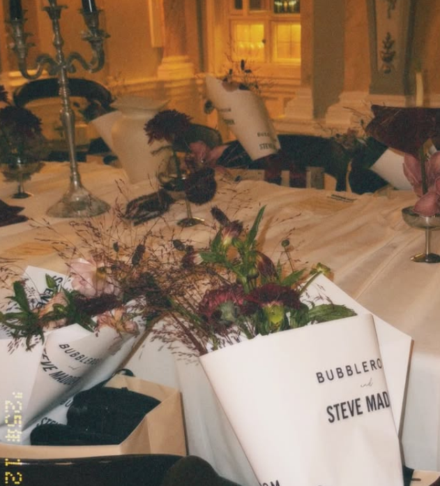 En festplanering med blomsterarrangemang, vimplar och duk på ett elegant bord i ett gult utomhusmiljö.