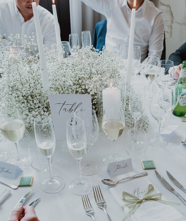 Bröllopss befintlig bord med vitt linnetygsduk, blommor, ljus, glas och bestick.