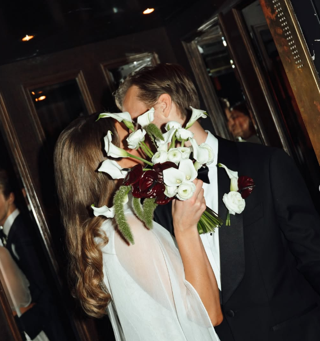 Brudpar som kysser varandra med en blomsterbukett framför ansiktena.