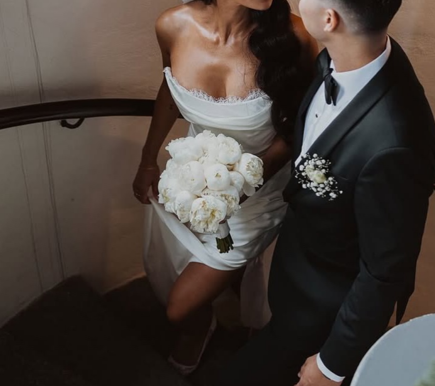 En brud och brudgum på en dansmanöver, brudens klänning och bukett av vita blommor syns tydligt.