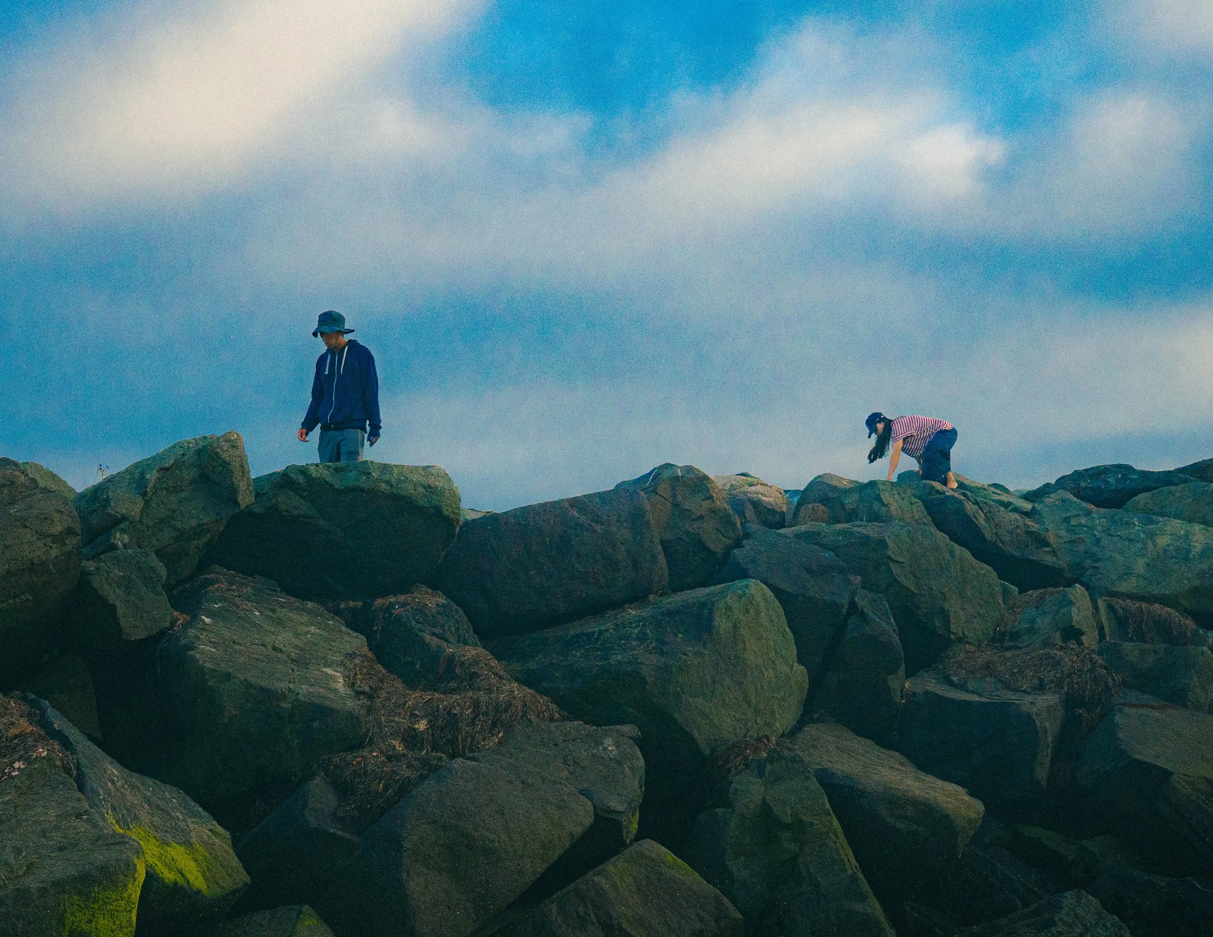 People exploring rocks on a beach with a cloudy sky overhead.