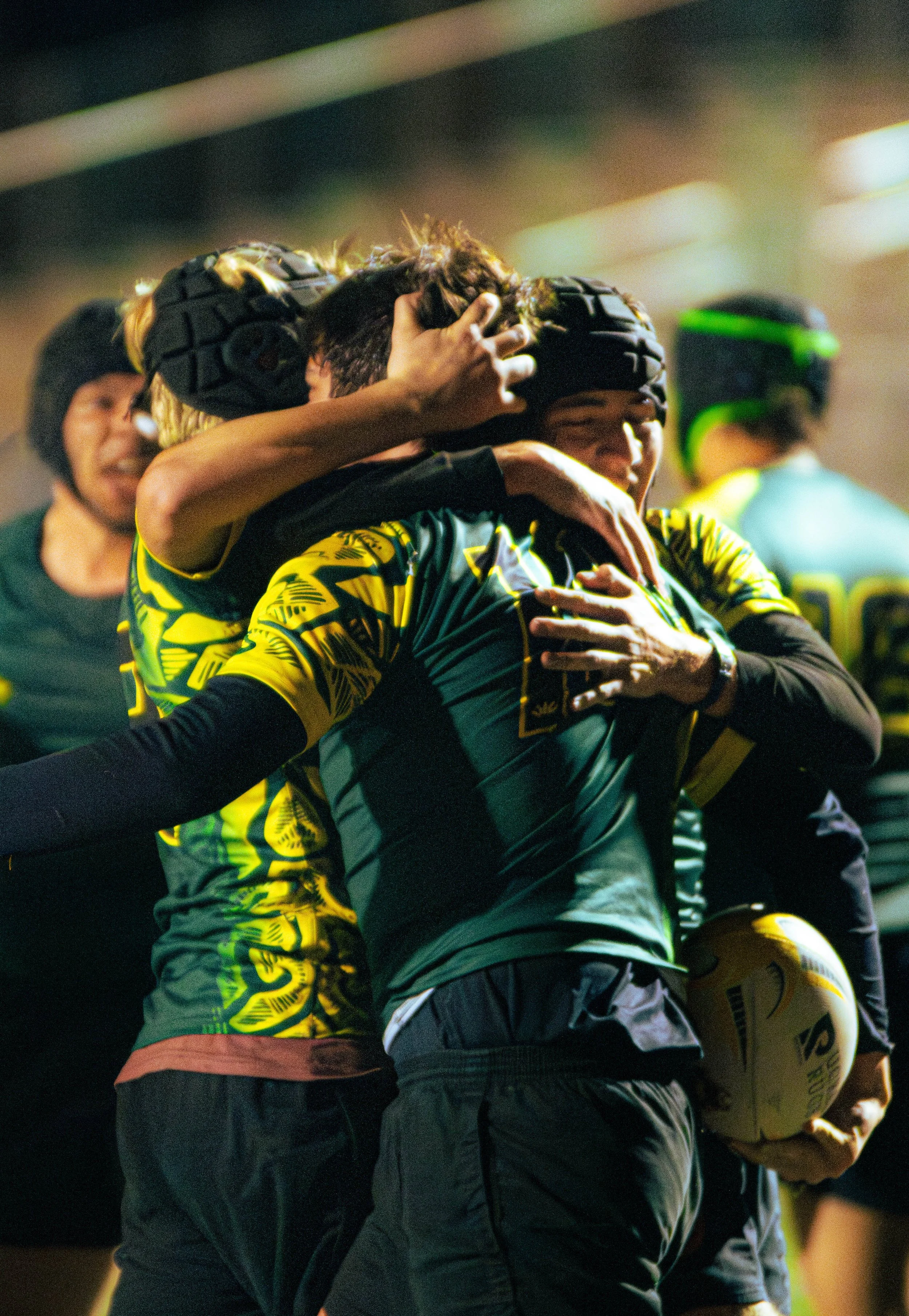 A group of rugby players in yellow and black uniforms celebrating on the field, with one player holding a rugby ball.