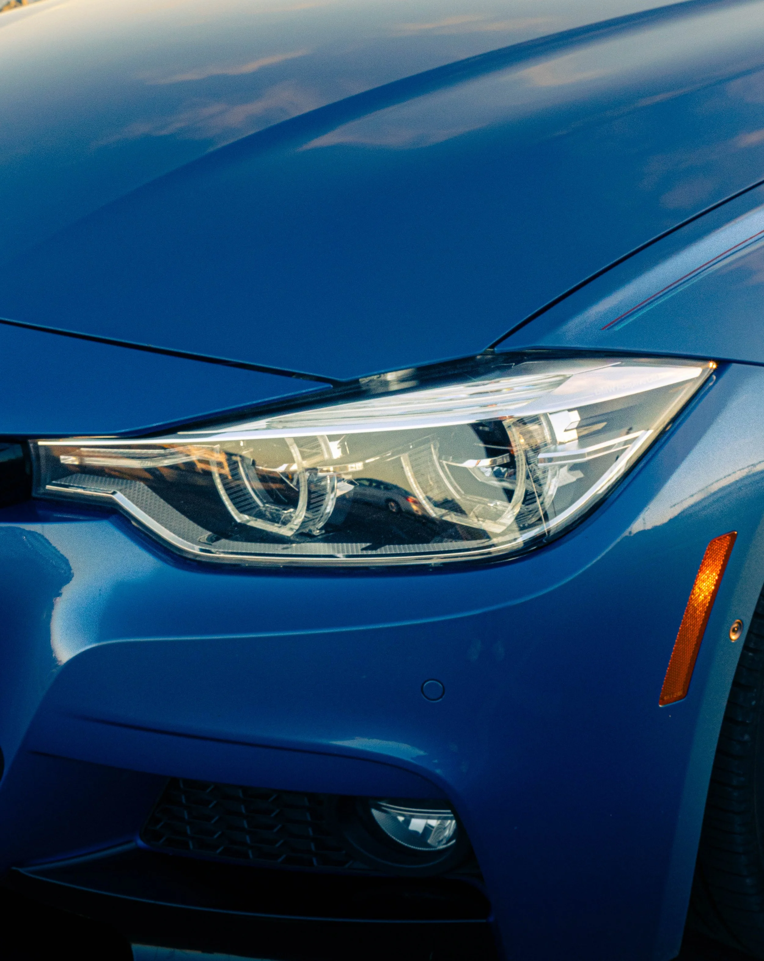 Close-up of a blue car's front left side, showing the headlight, grille, and part of the hood.