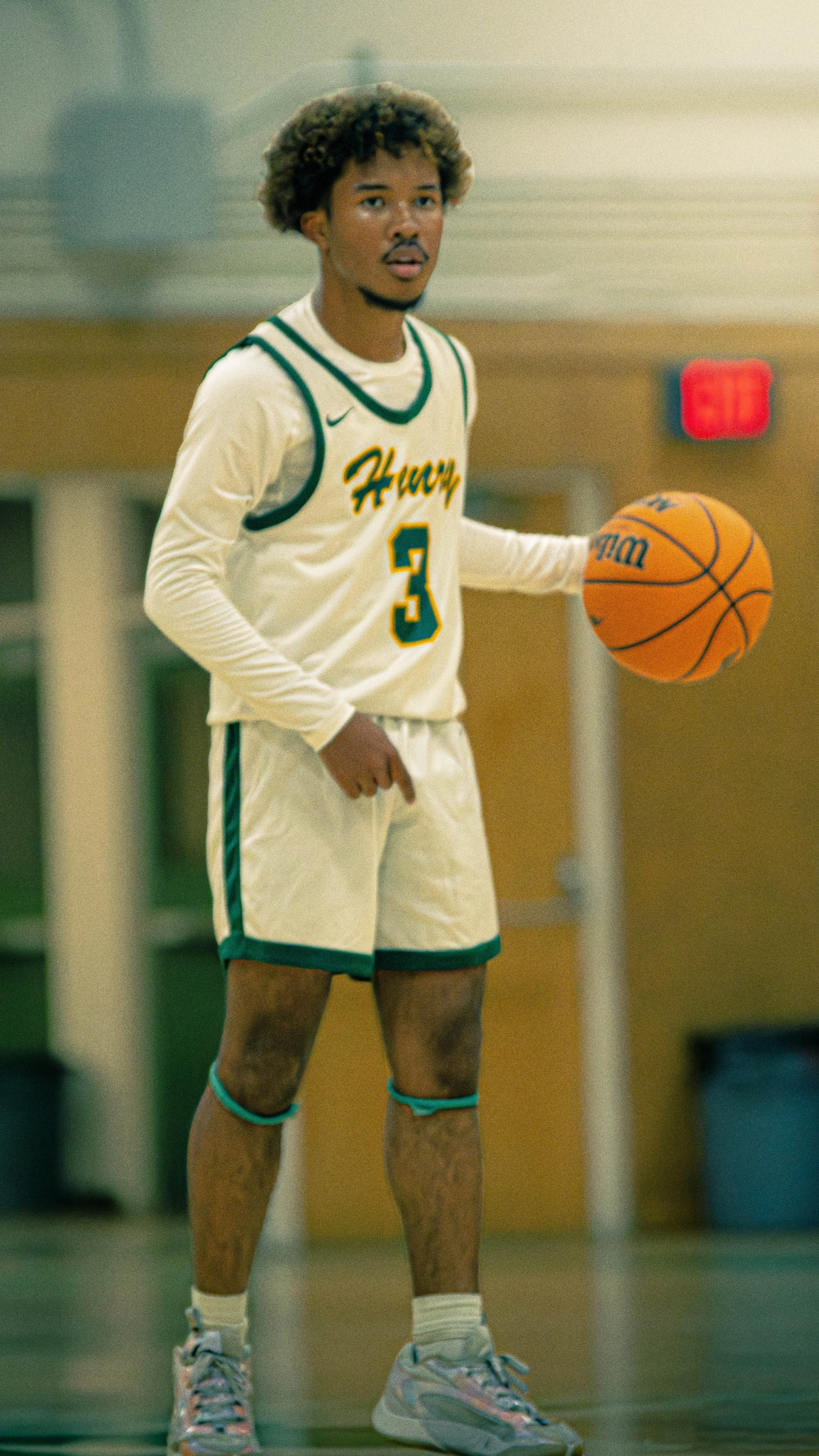 A young man in a basketball uniform holding a basketball, standing on a court inside a gym.