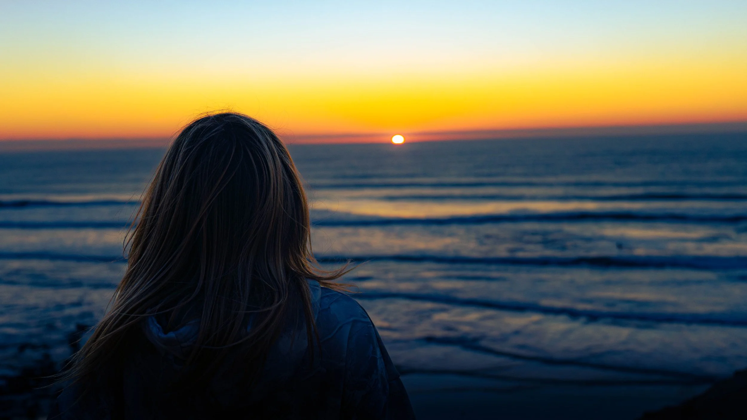 Person with long hair looking at sunset over the ocean