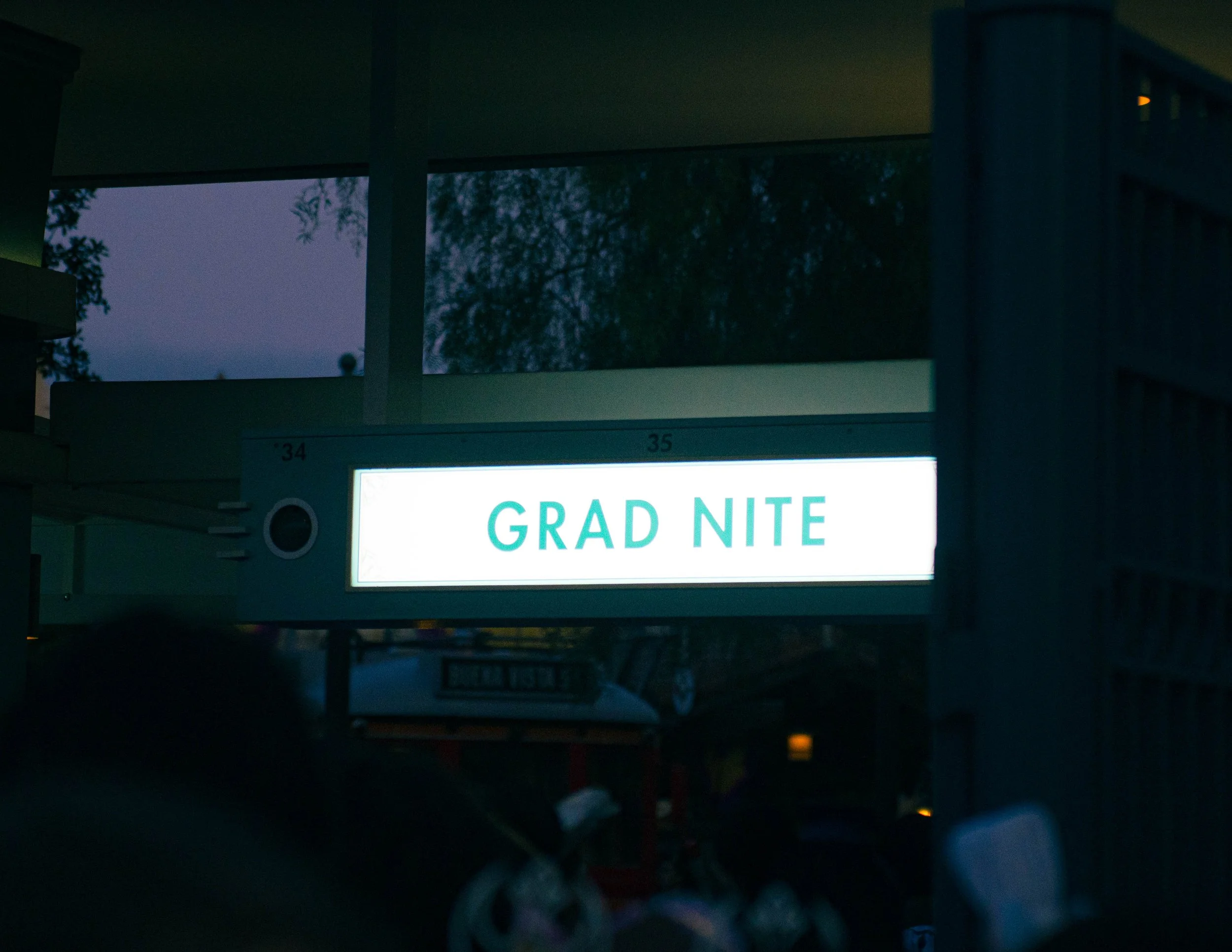 Nighttime outdoor scene with a lit sign reading 'Grad Nite' and trees visible in the background.