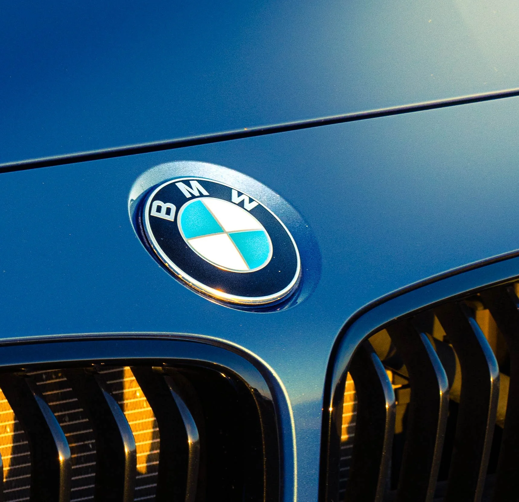 Close-up of a BMW emblem on a blue car's grille, highlighting the chrome and black grille details.