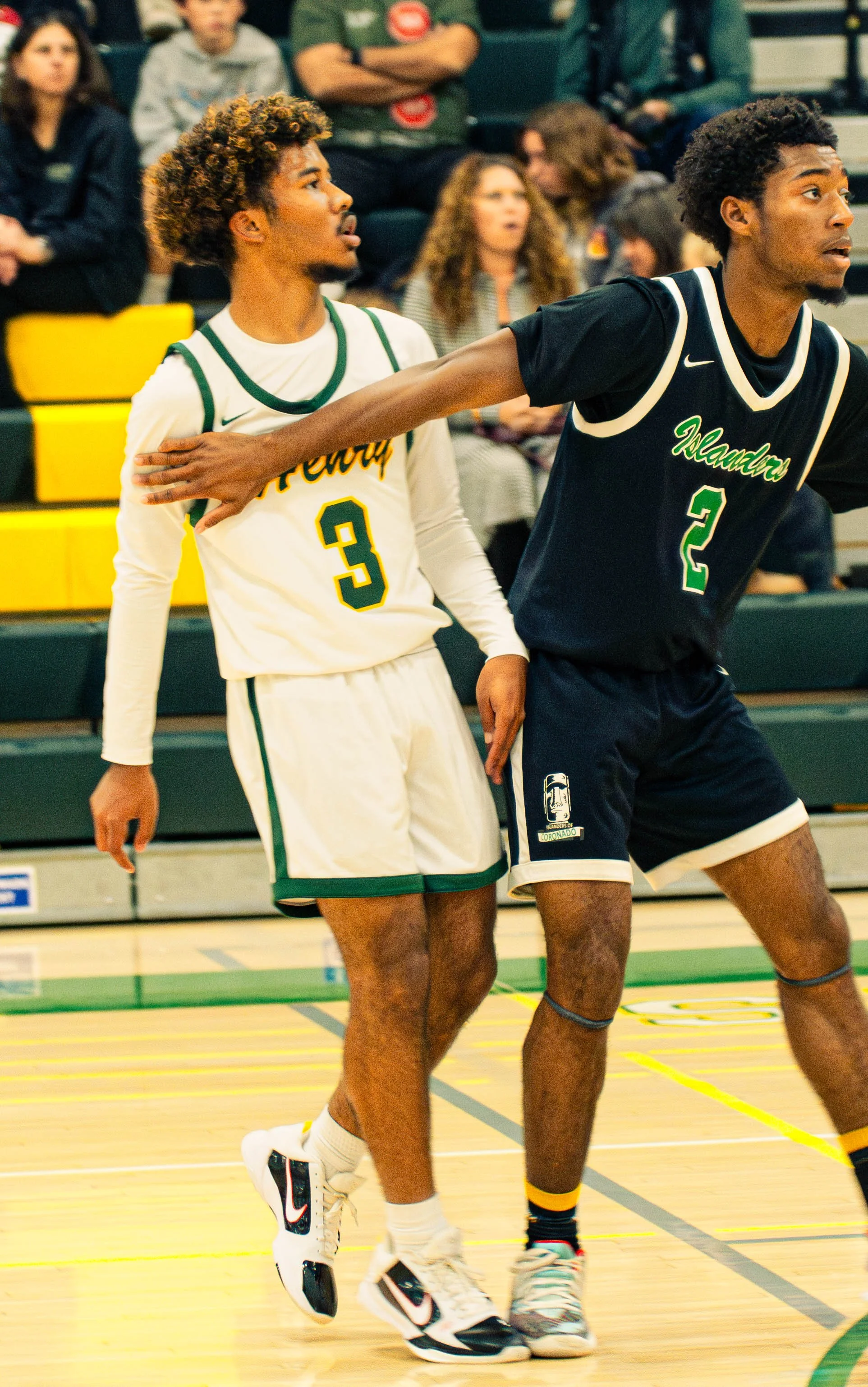 Two basketball players on a court, one wearing a white jersey with the number 3, and the other wearing a black jersey with the number 2, engaged in a game.