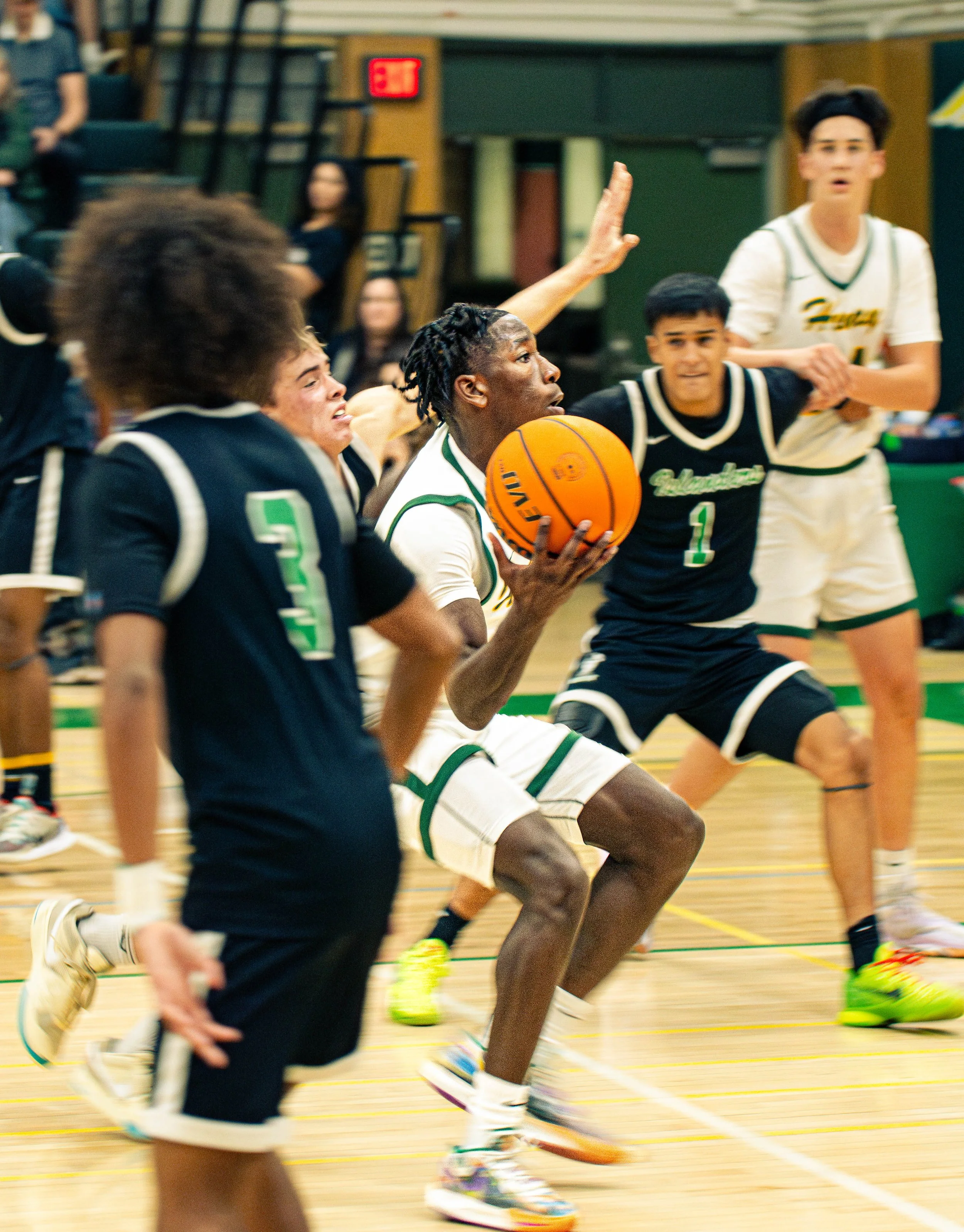 A group of young people playing basketball in an indoor gymnasium. They are wearing sports jerseys and are actively engaged in the game, with some players running and one player holding the basketball.