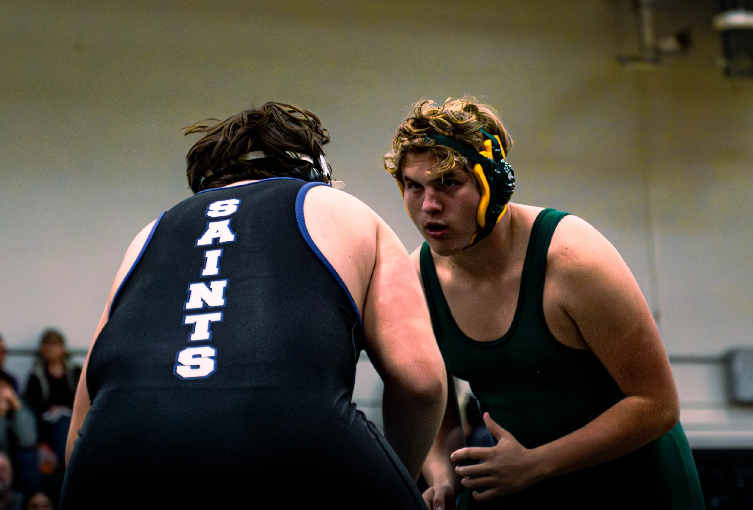 Two wrestlers face each other in a match, both wearing headgear and athletic gear, focused on each other.