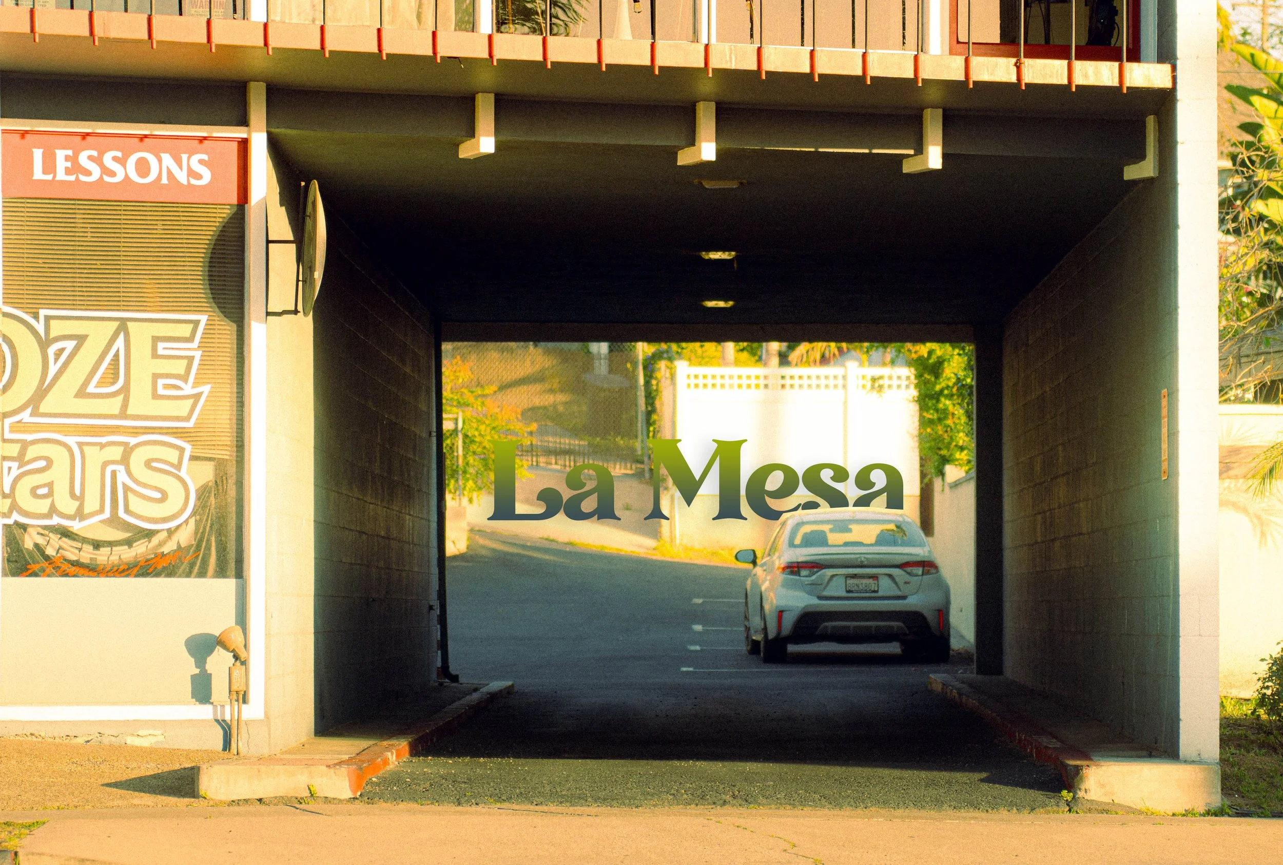 Underpass with a parked car and a sign that says 'La Mesa. The underpass has a dark ceiling with small lights and is surrounded by trees and buildings.