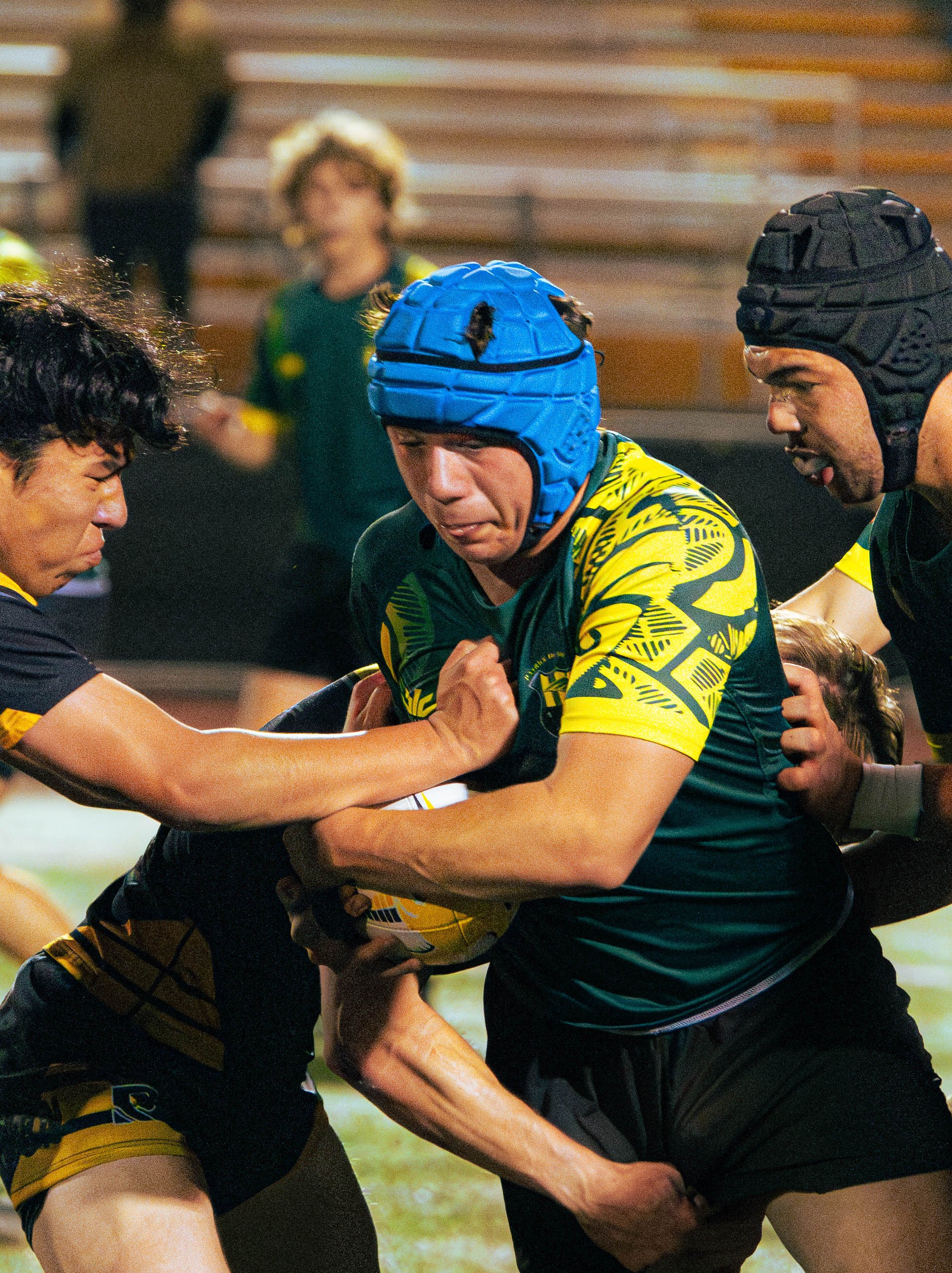 Two rugby players wearing protective headgear and jerseys competing in a match while two referees intervene.