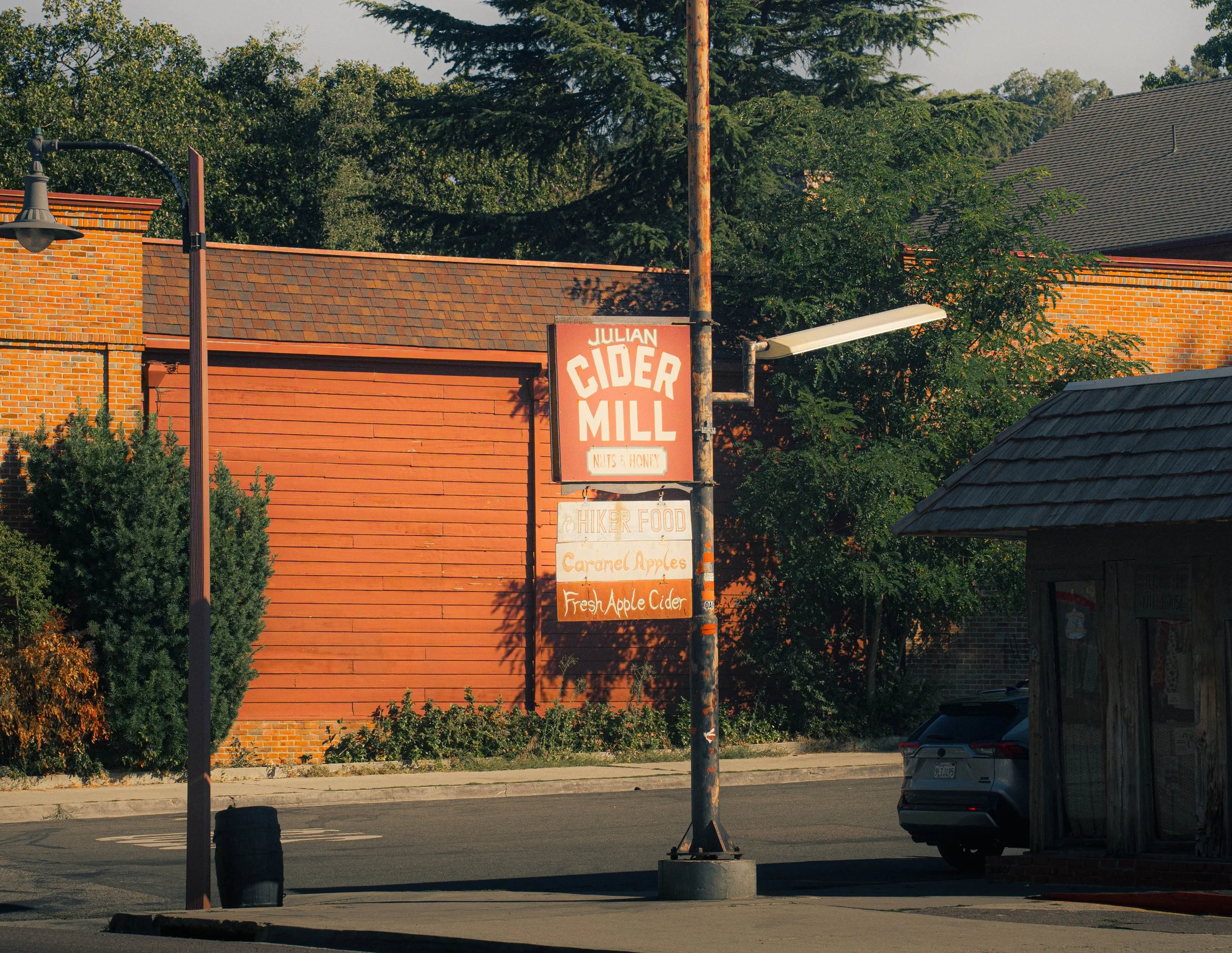 A street view with a brick building, a sign for Julian Cider Mill, trees in the background, and a parked car.