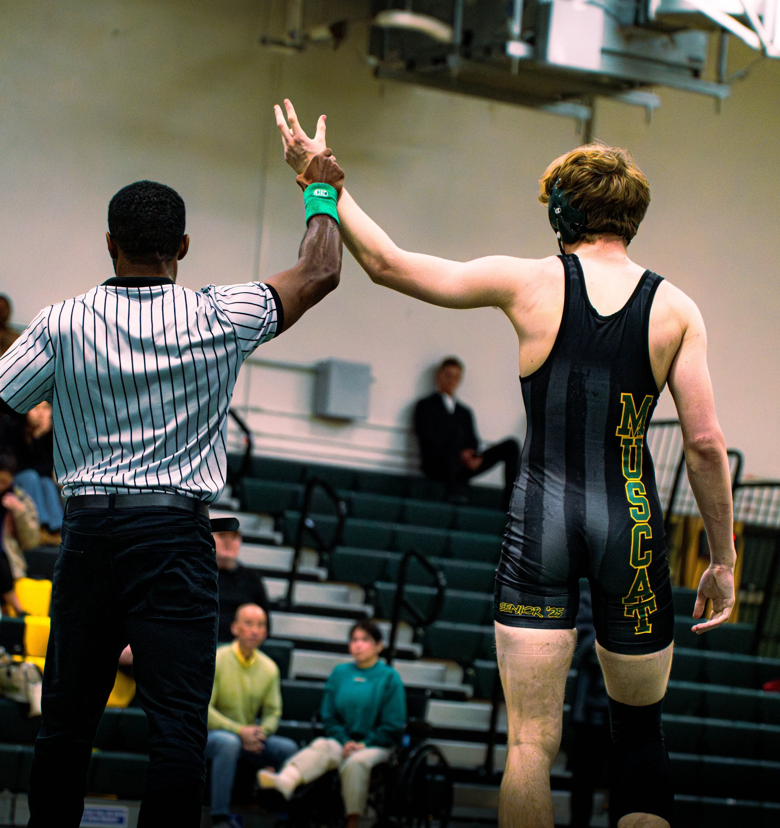 A female volleyball player wearing a black jersey with yellow and green lettering, and a male referee in a black and white striped shirt, high-fiving in an indoor gymnasium with spectators in the background.