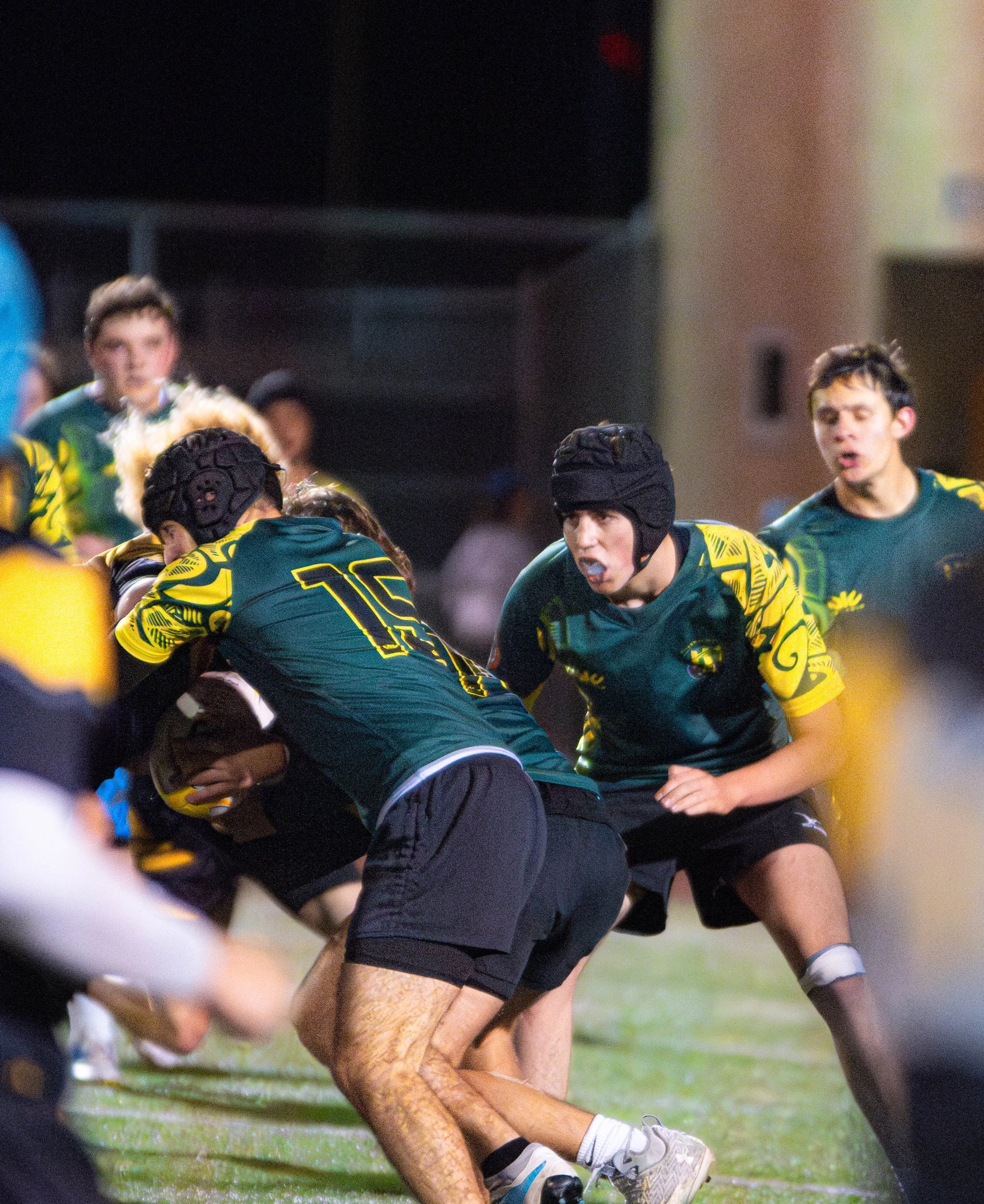 Lacrosse players competing during a game, wearing helmets and uniforms in yellow and green, engaged in a physical struggle on the field.