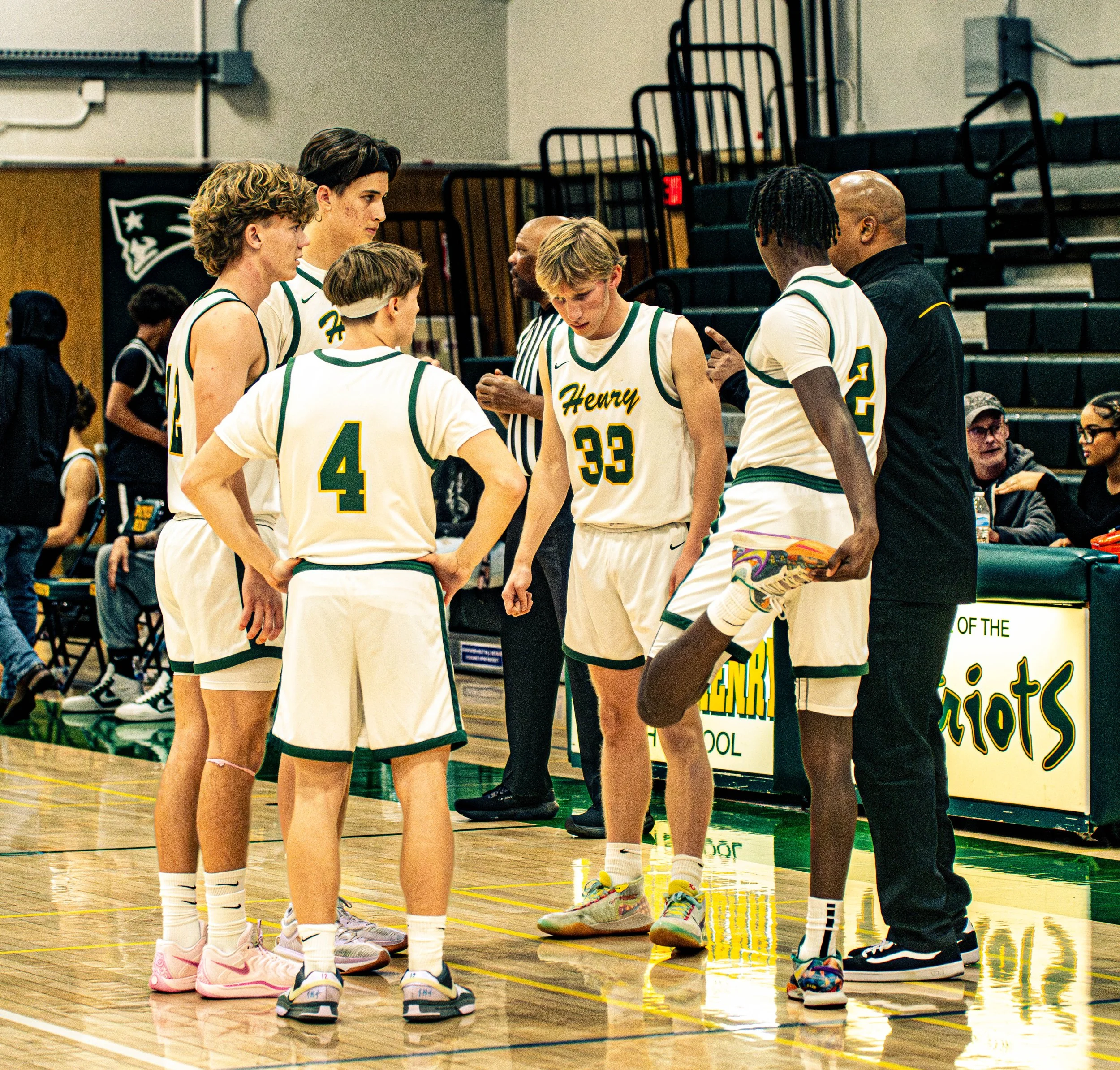 A group of high school basketball players in green and white uniforms huddle during a game or practice in a gymnasium.