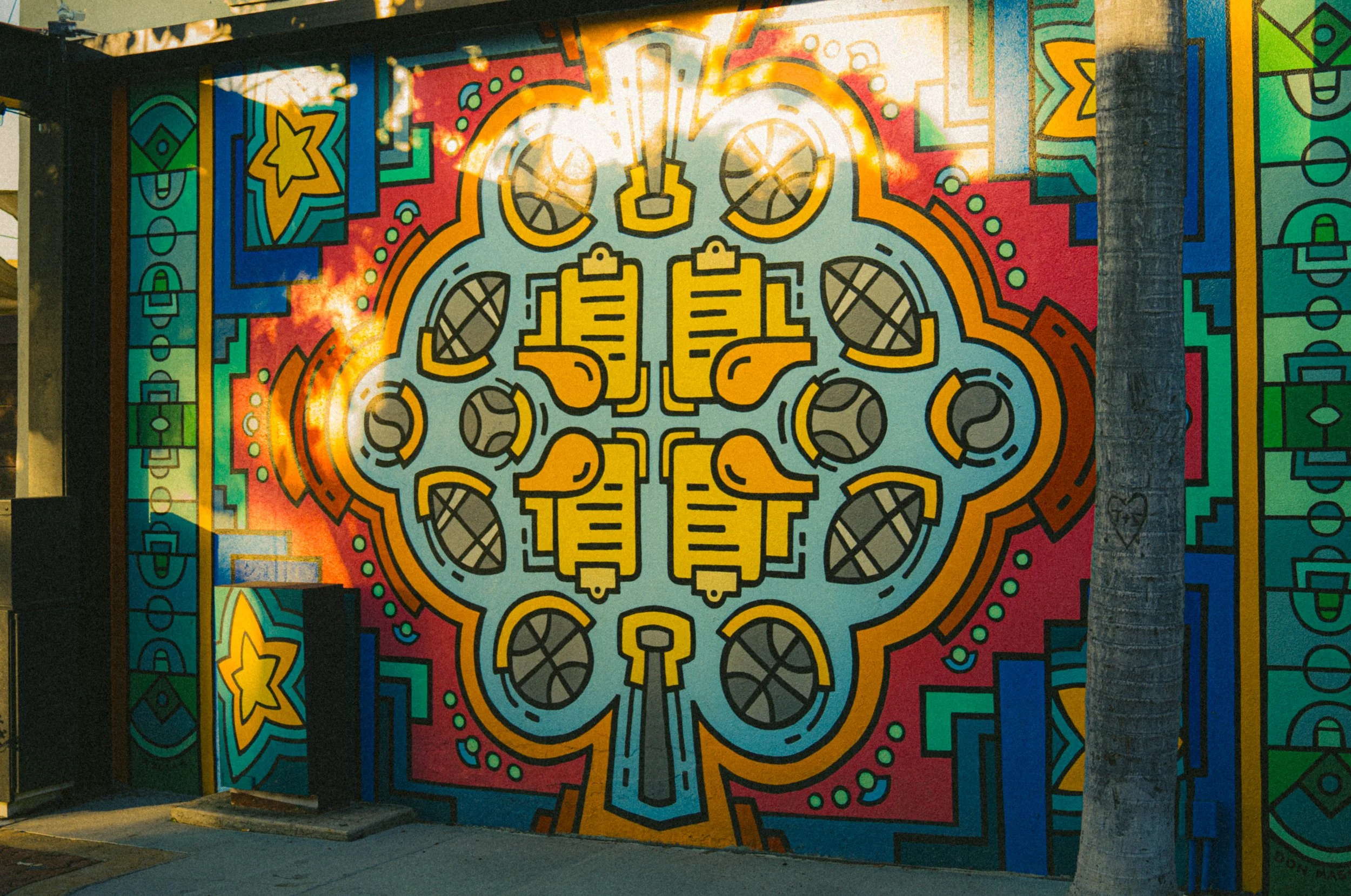 Colorful mural with abstract shapes, yellow and black elements, and a background with various bright colors including red, green, and blue, painted on a building exterior.