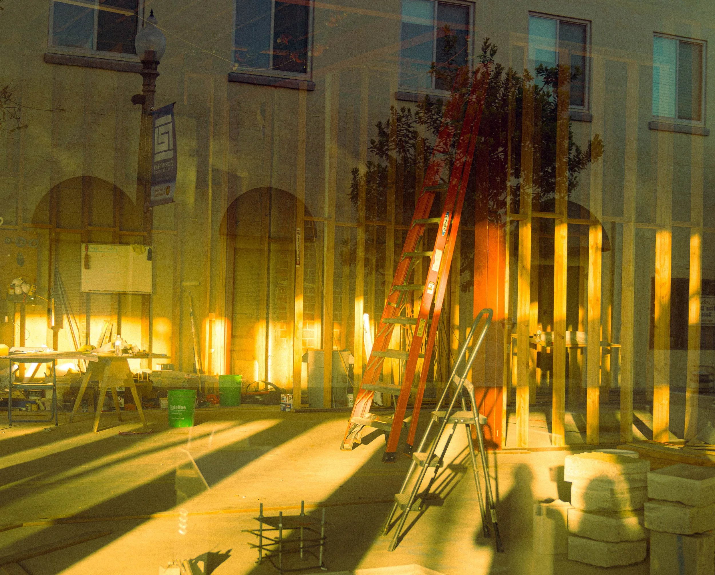 Construction site with wooden framing, ladders, tools, and supplies, illuminated by construction lighting.