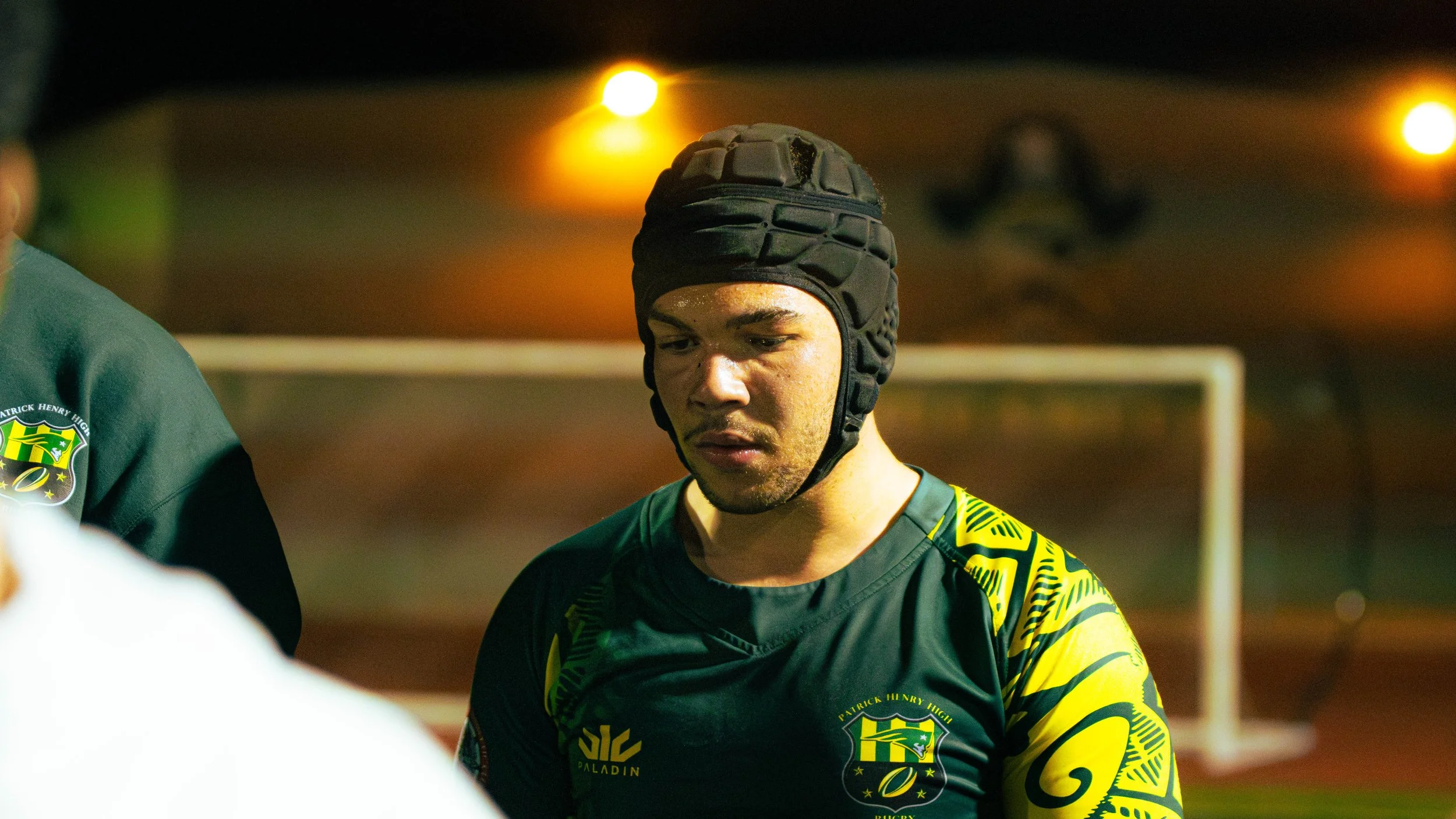 Cricket player with black protective helmet and green sports jersey during a game at night.
