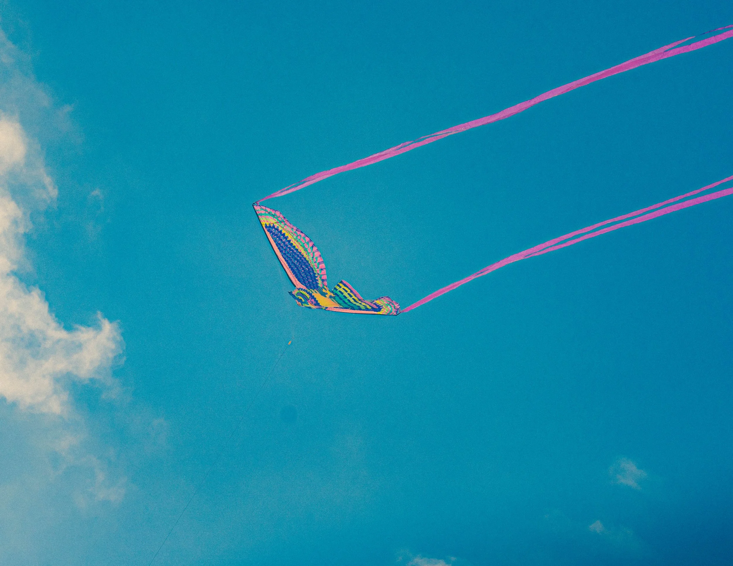 Colorful kite flying in a blue sky with clouds.