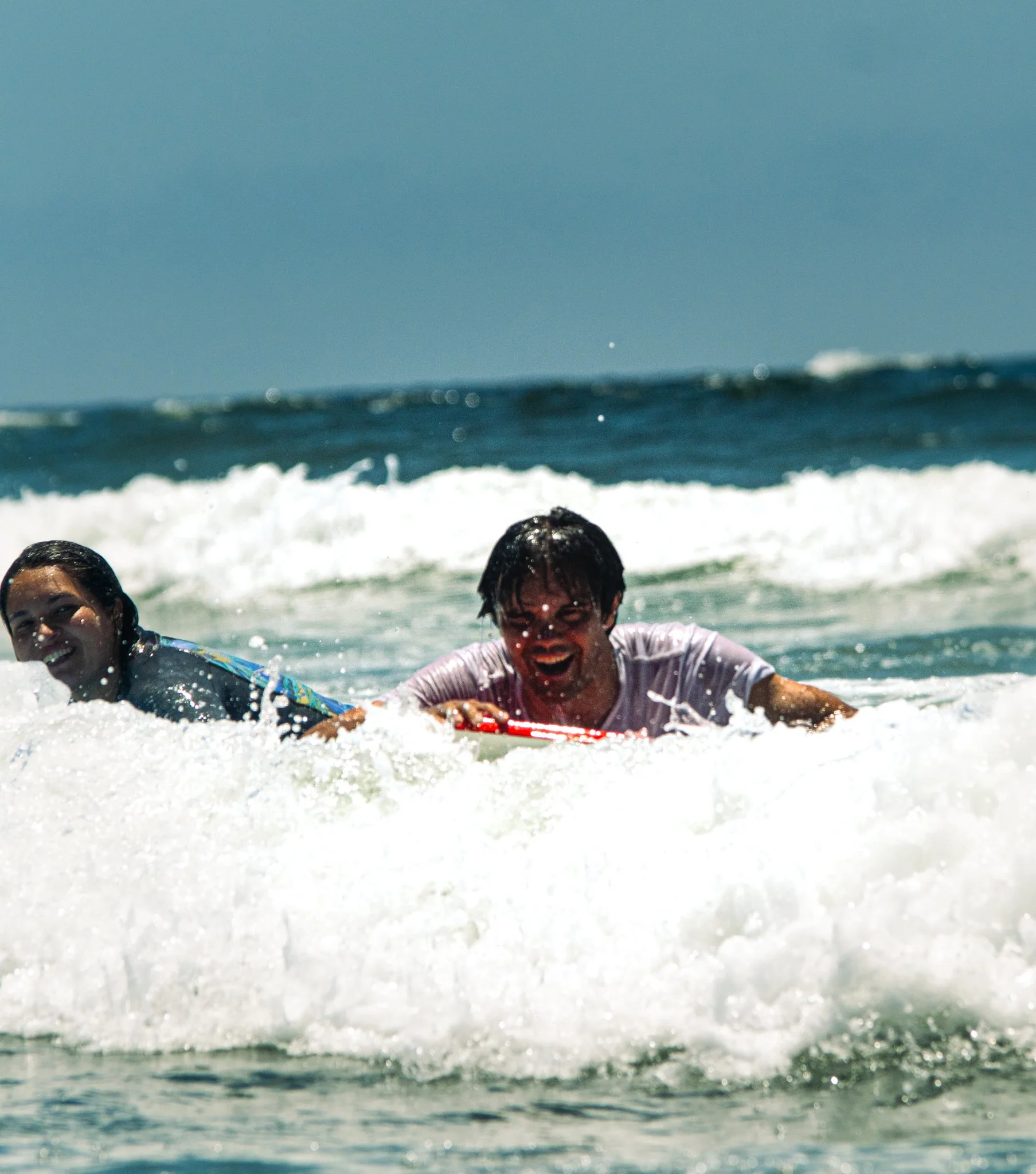 People enjoying themselves in the shallow ocean water, smiling and playing, with waves and a clear sky in the background.