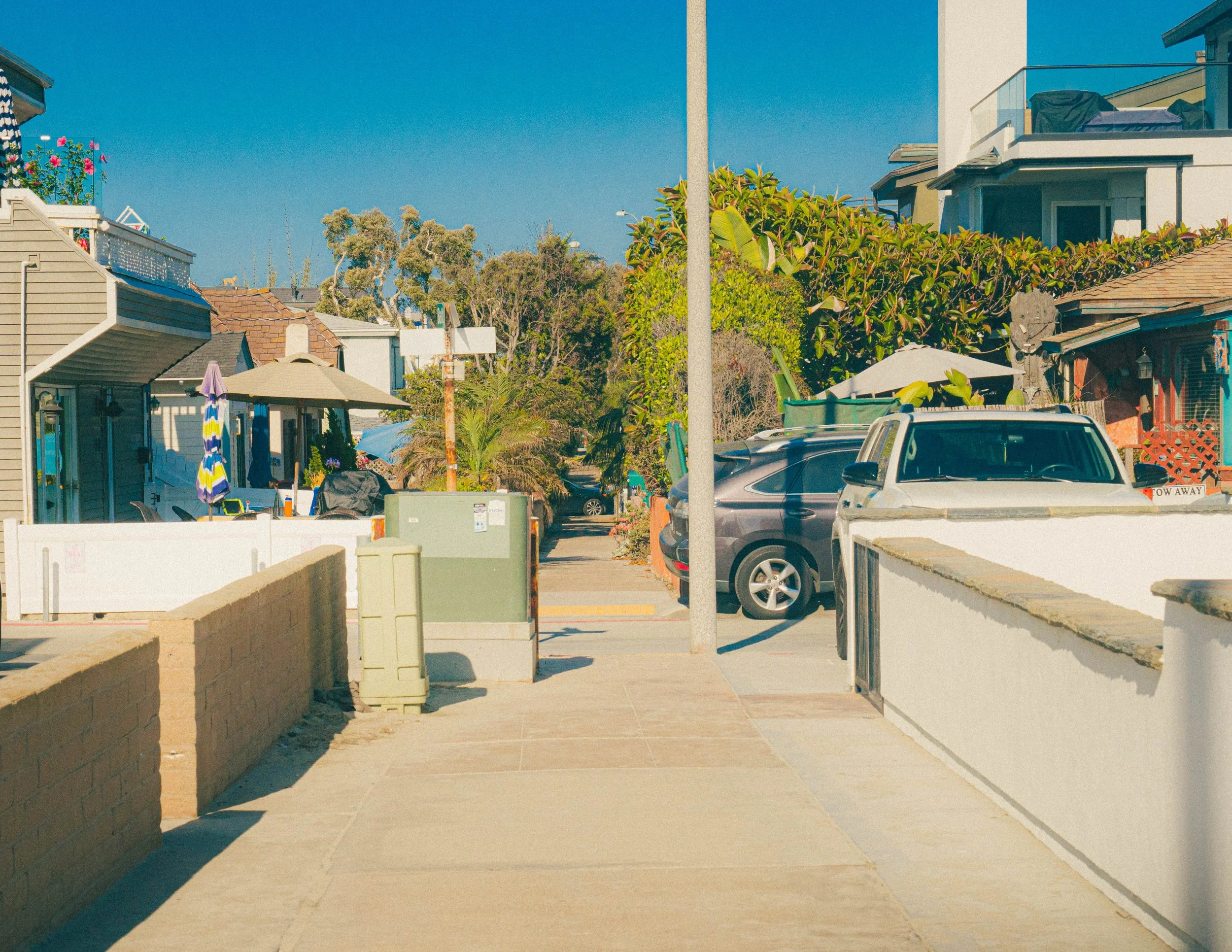 Residential neighborhood with houses, parked cars, a clear blue sky, and greenery.