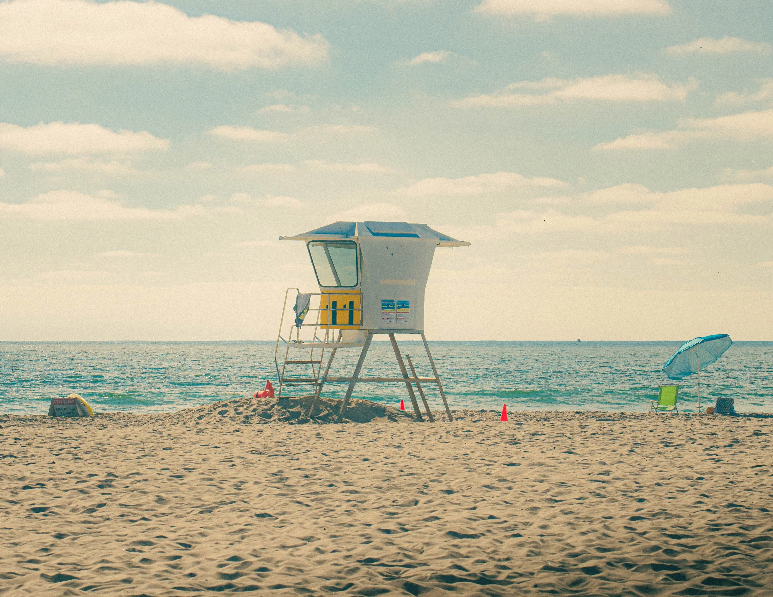 A lifeguard tower on a sandy beach with a partly cloudy sky in the background.