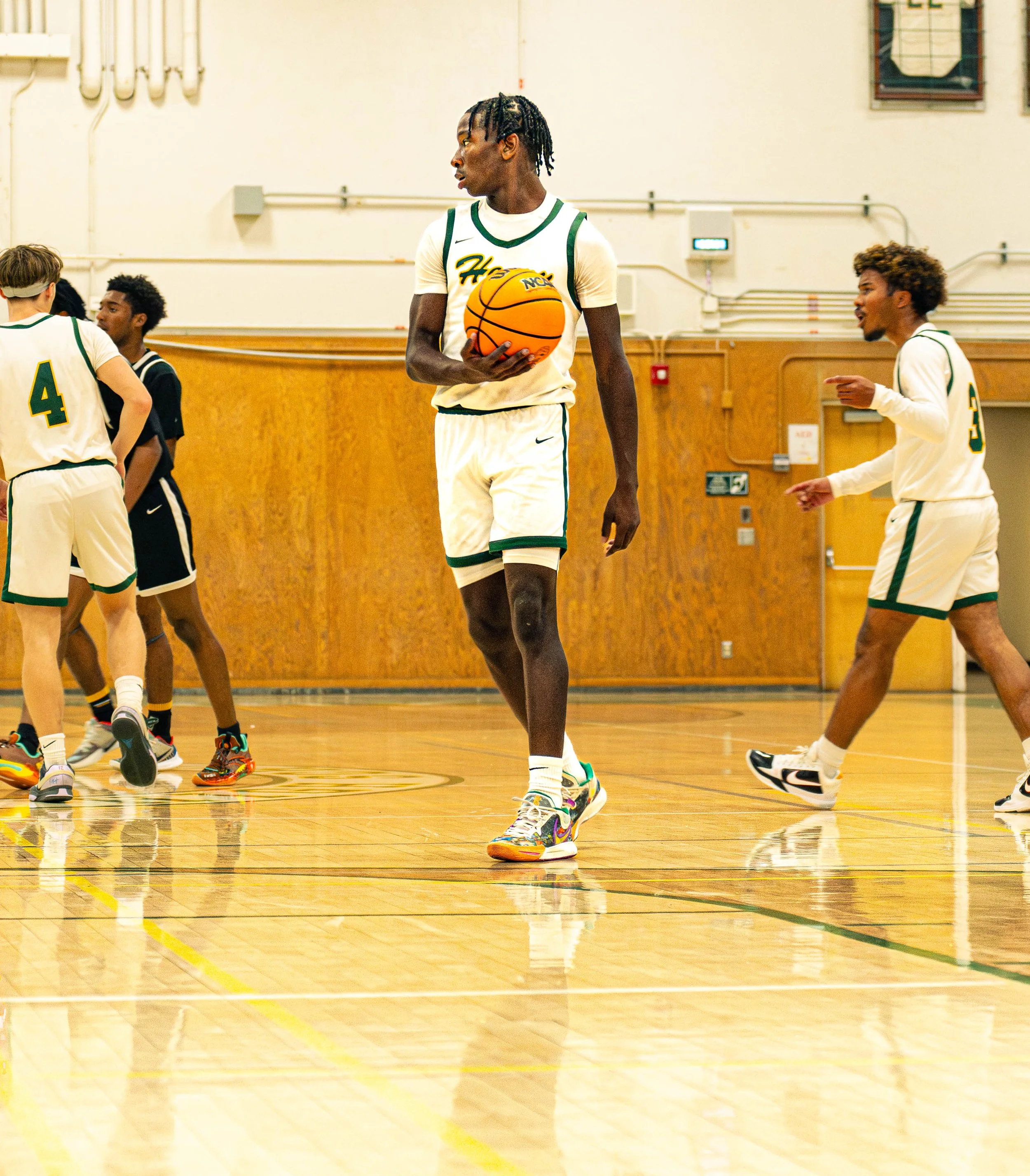 A basketball player holding a basketball on a gym floor with other players nearby.