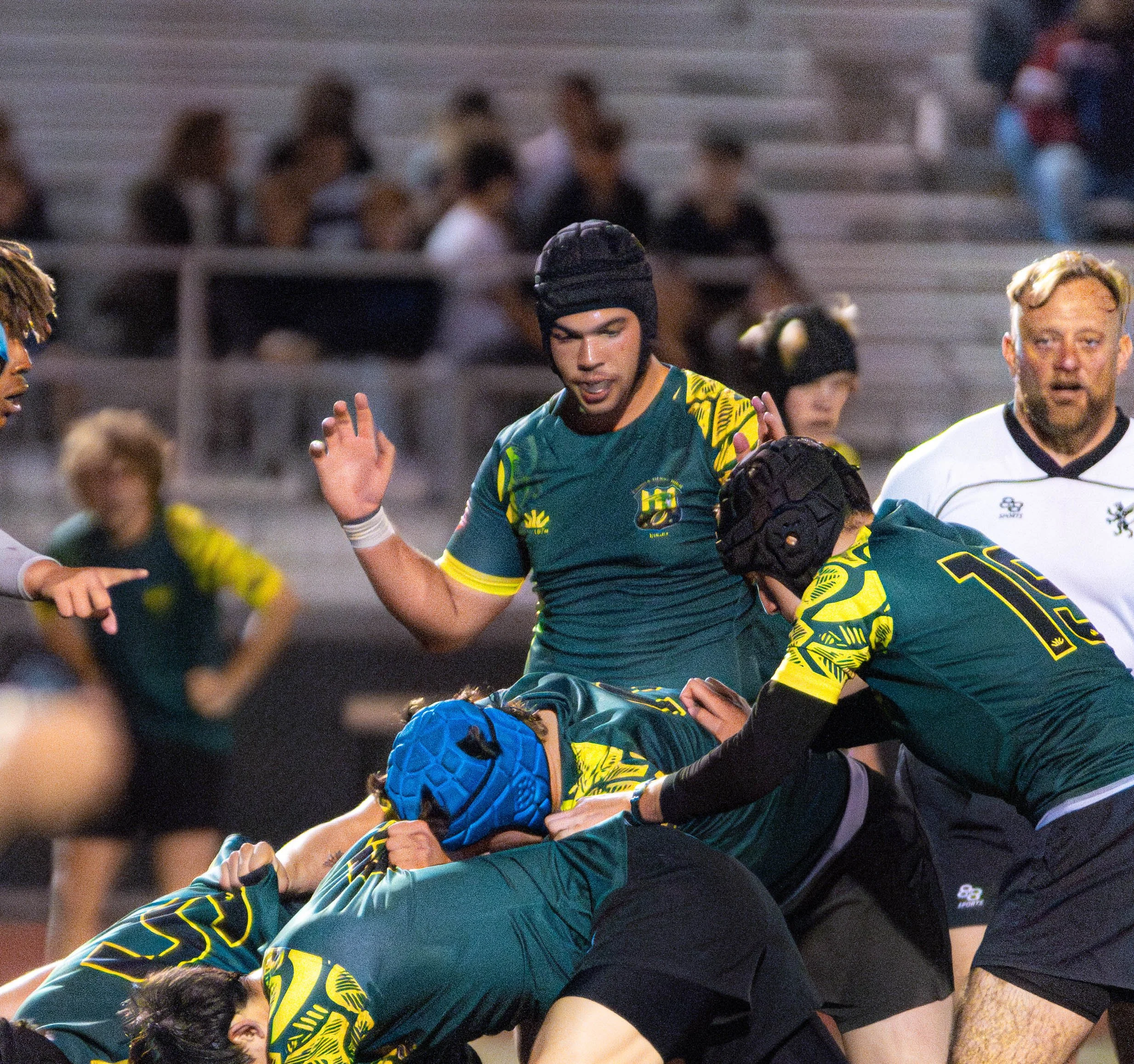 Rugby players in a scrum on the field during a game, with spectators in the background.