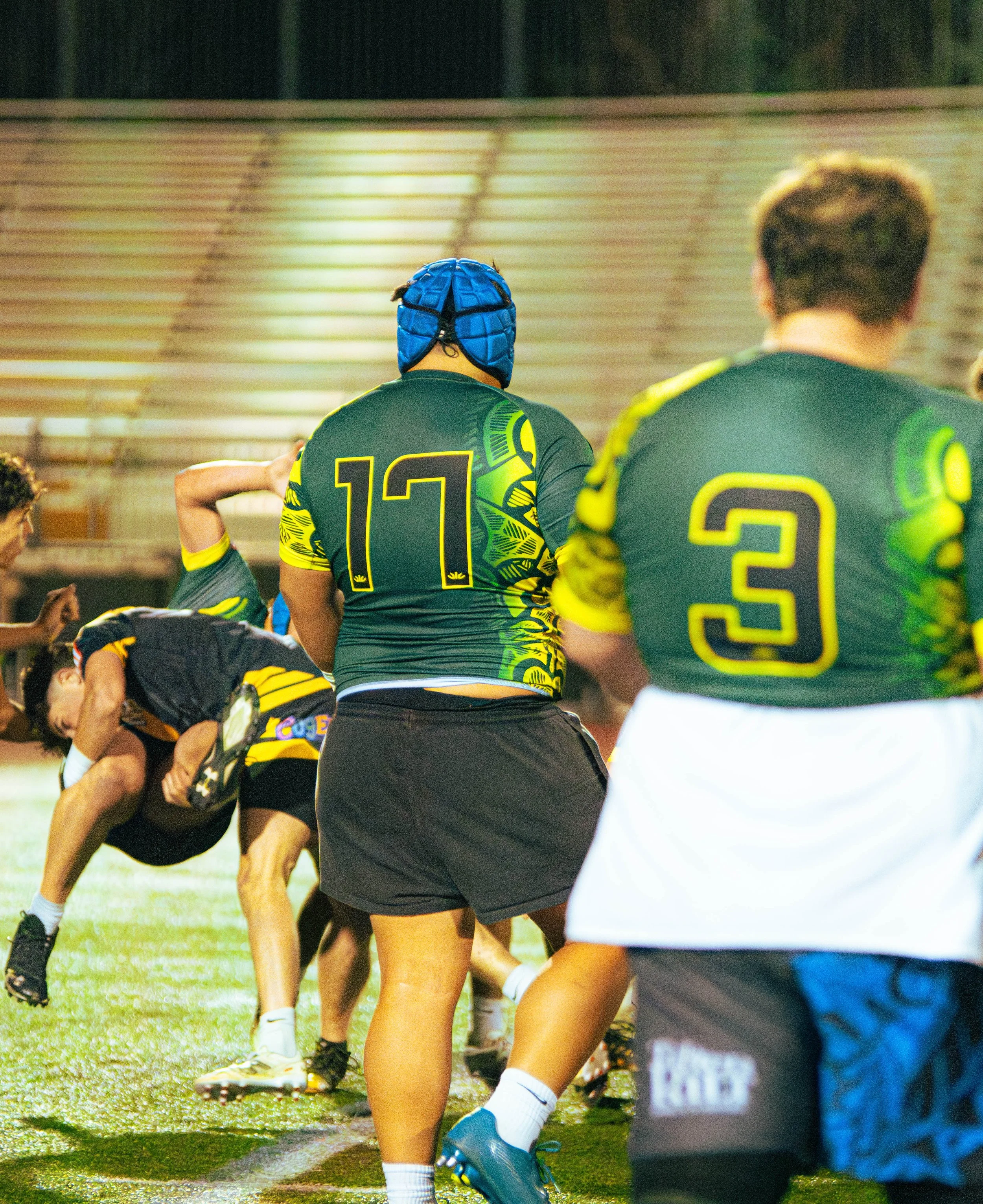 A group of rugby players in black and yellow uniforms forming a scrum on a grassy field, with some wearing protective headgear.