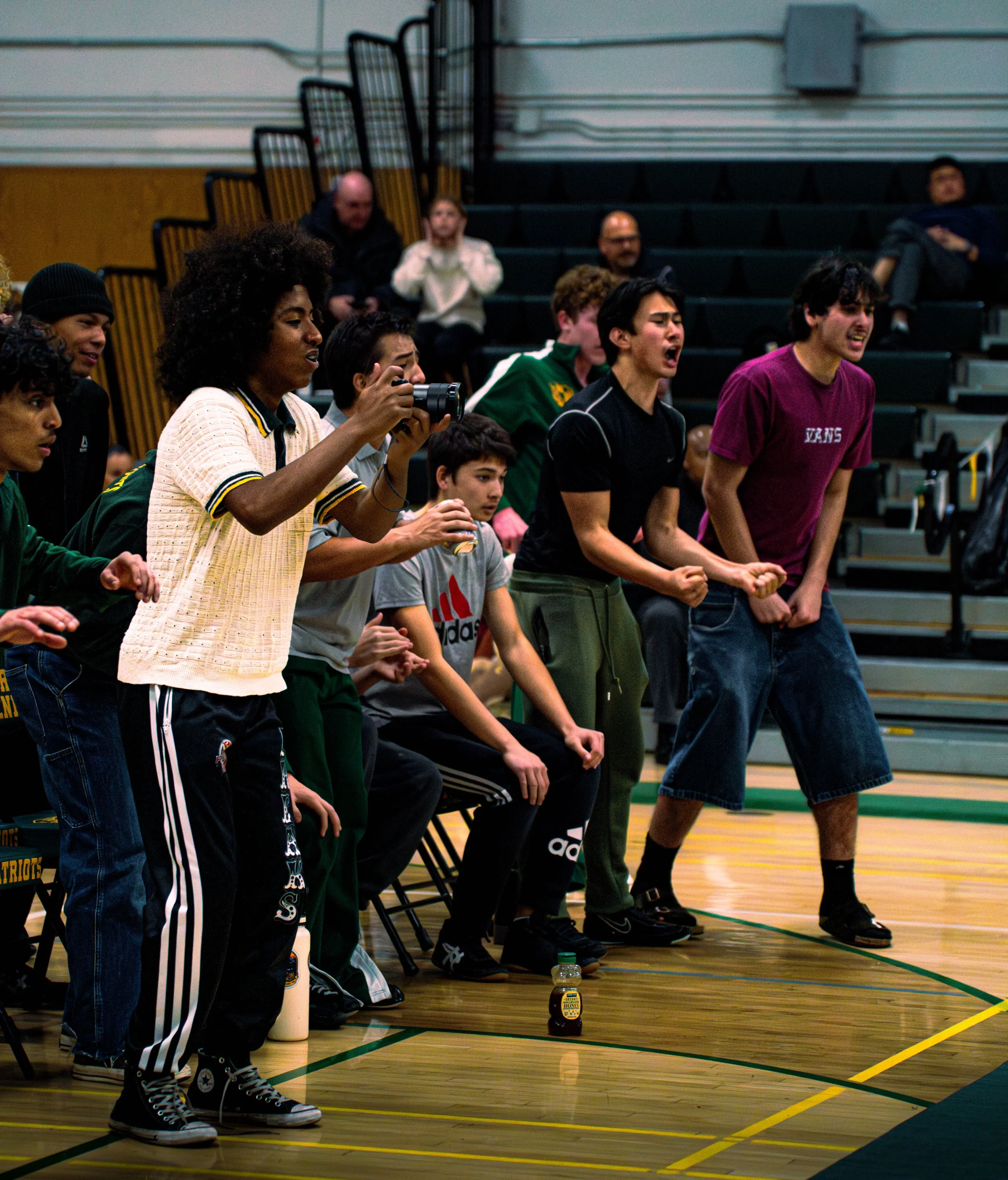 People standing and cheering in a gymnasium, possibly during a sports event, with chairs and a water bottle on the floor.
