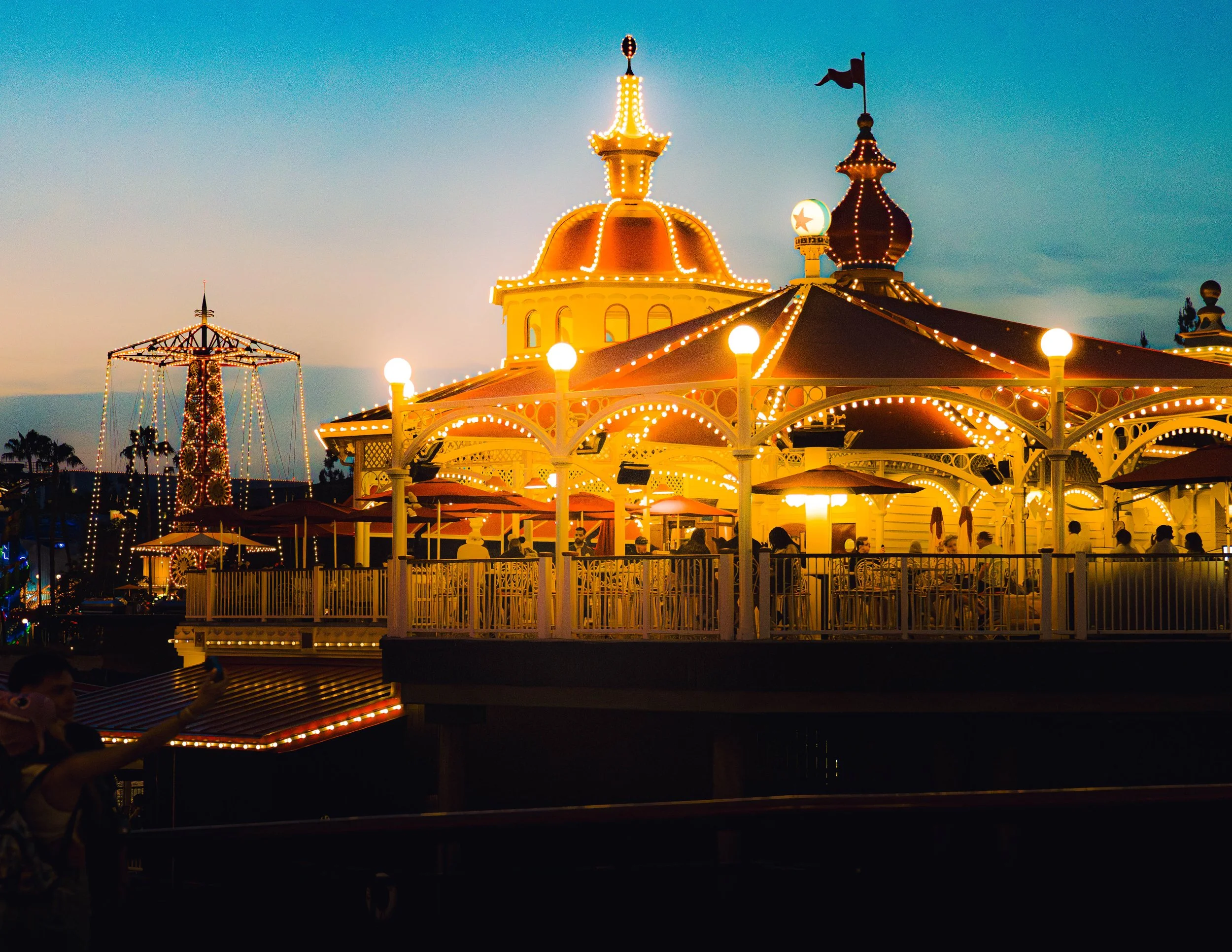 A brightly lit amusement park with a carousel, a tower ride, and a spinning ride at dusk.