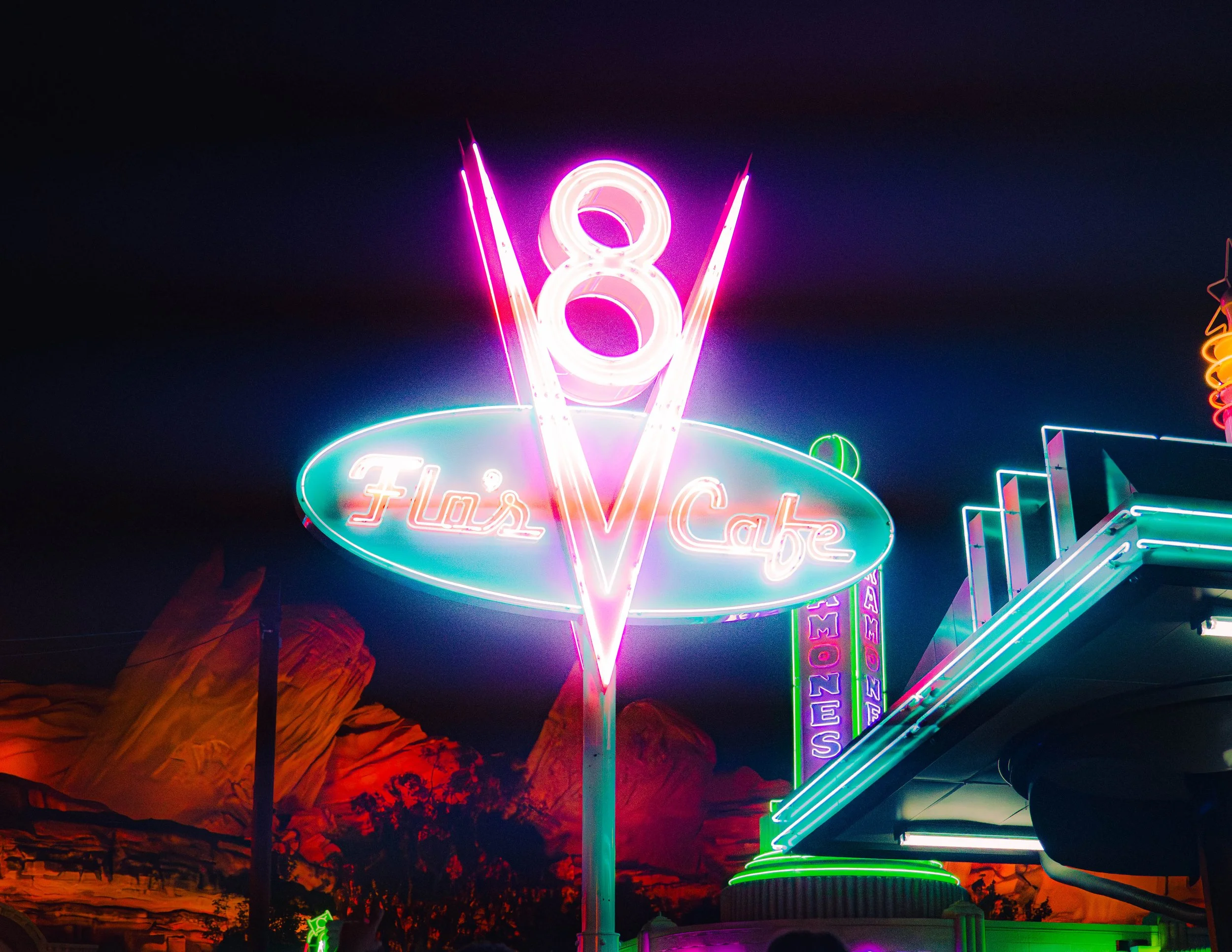Neon sign displaying the number 8 and a V, with a background of colorful lights and desert landscape at night.