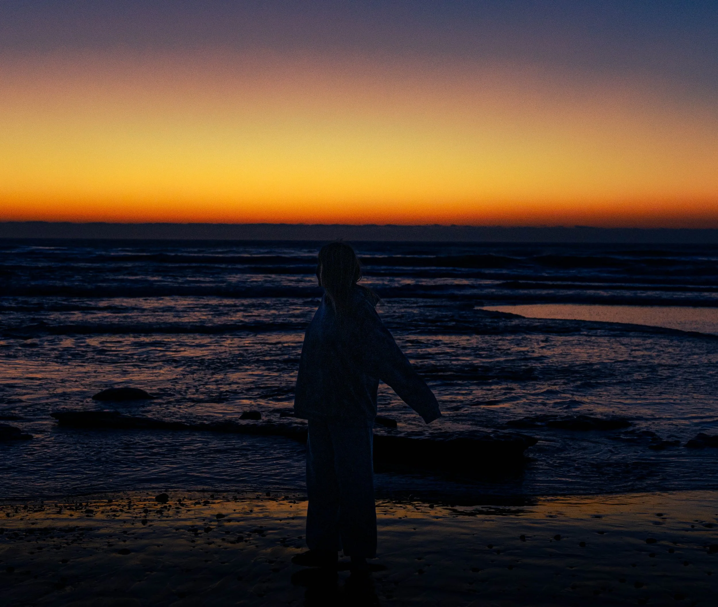 Silhouetted sculpture of a horse on the beach during a sunset with colorful sky and calm ocean waves.