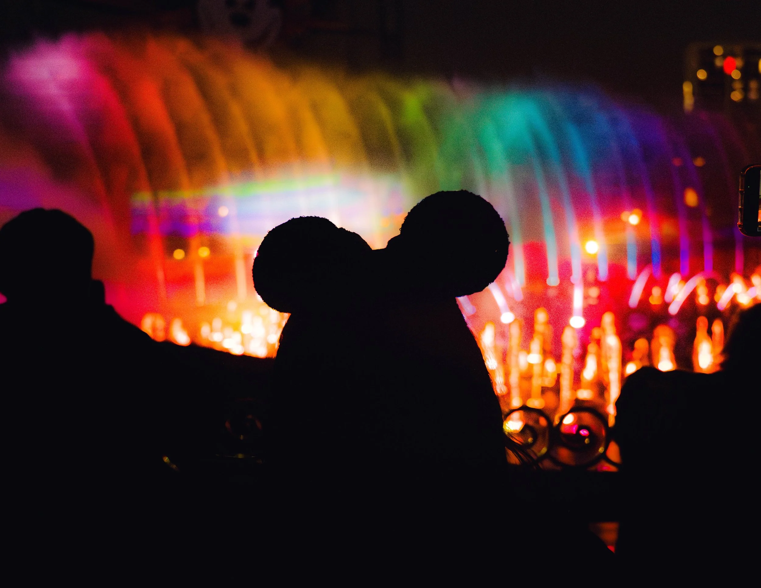 Silhouettes of two heads watching a vibrant fireworks display in various colors against a dark night sky.