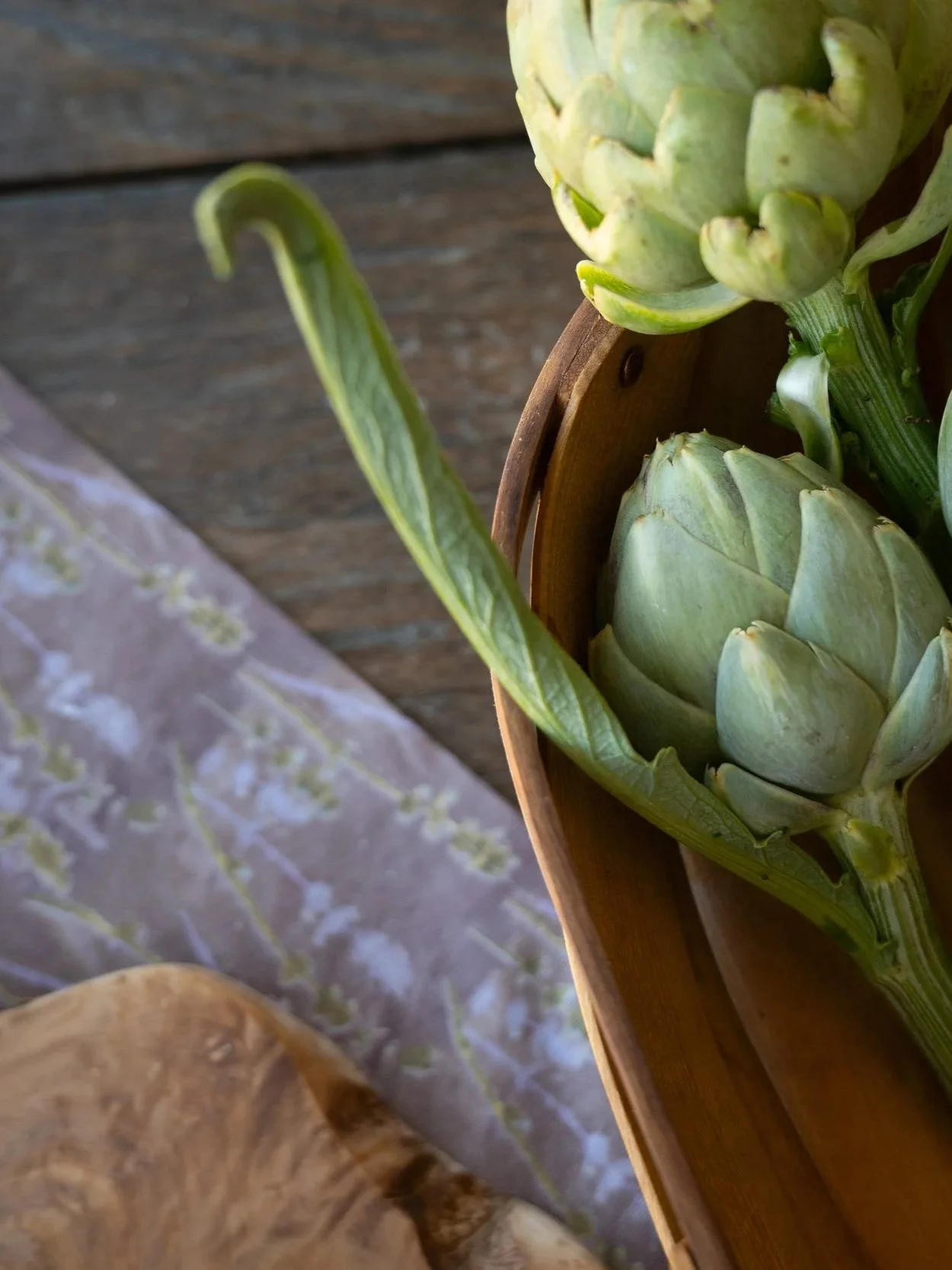 Fresh green artichokes in a wooden bowl on a rustic wooden surface.