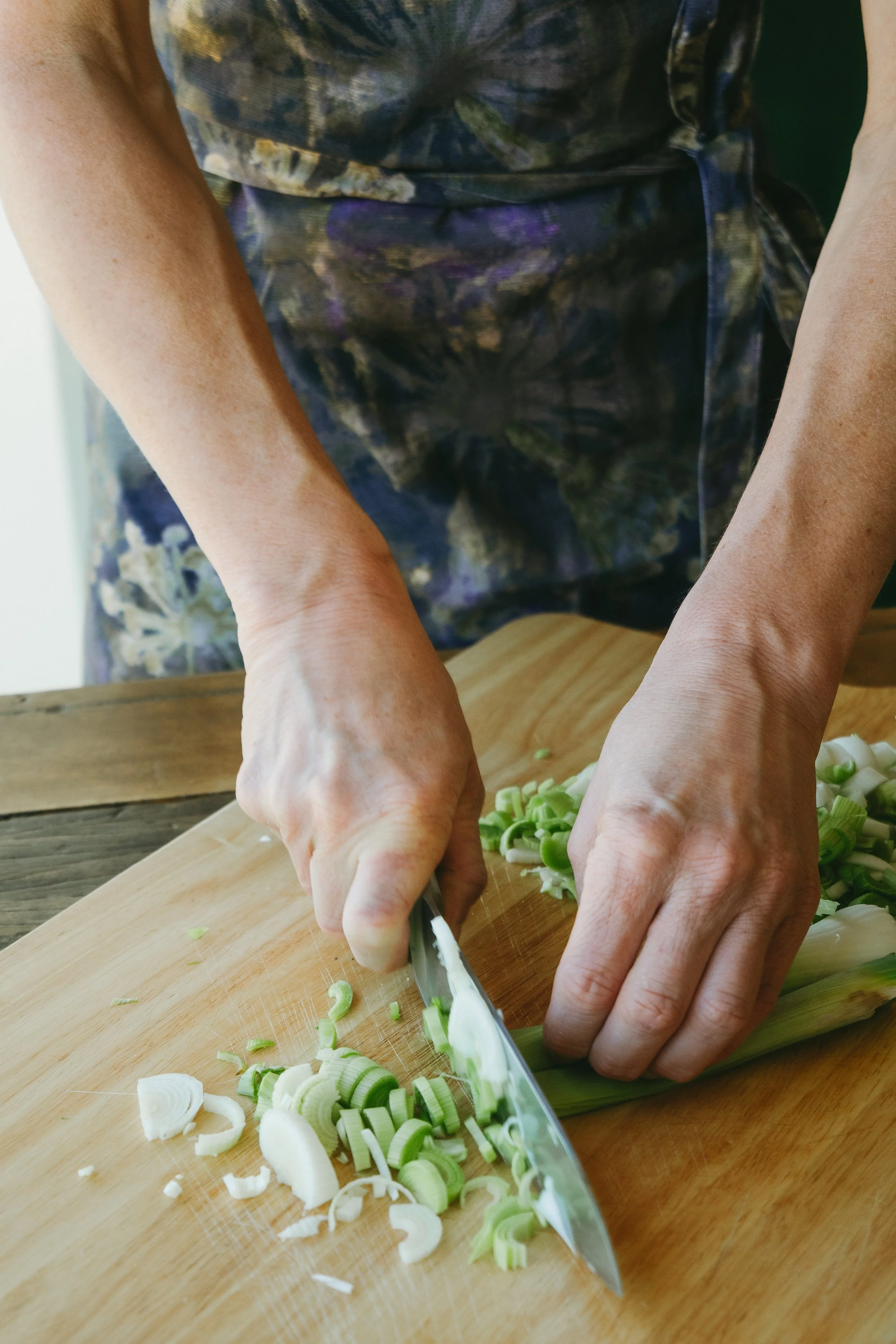 Close-up of a person chopping green onions on a wooden cutting board with a large knife.