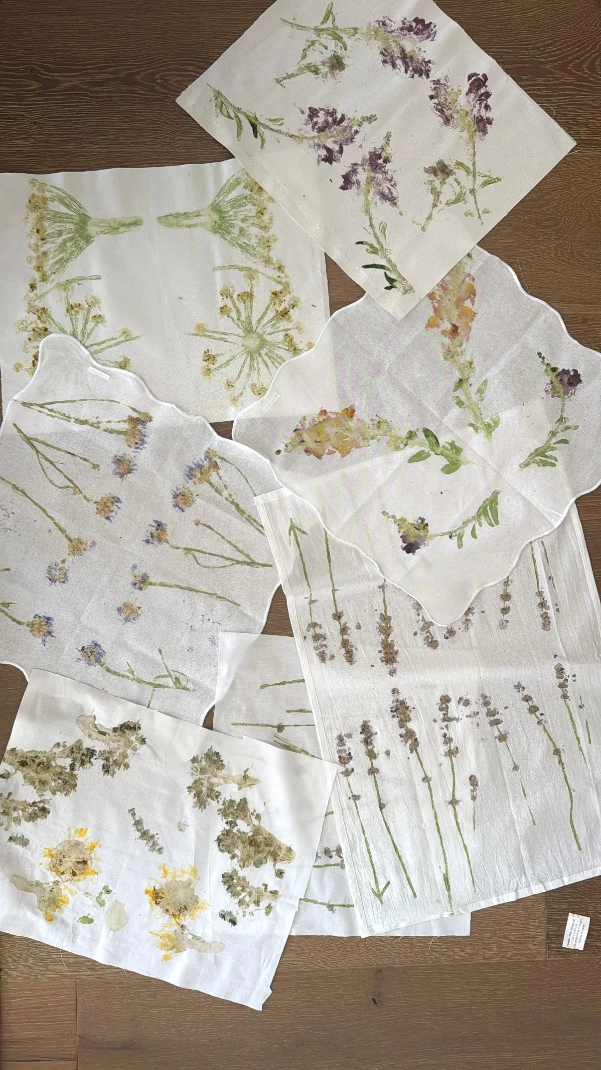 Assorted sheets of paper with pressed and painted flowers and plant illustrations, spread out on a wooden floor.