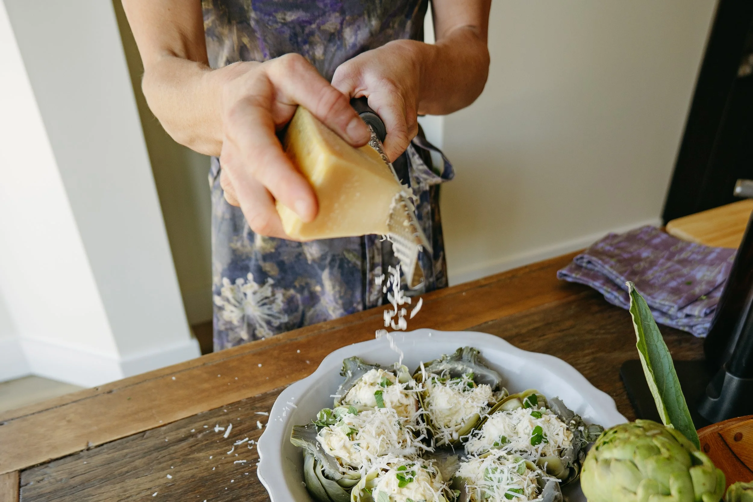 Person grating cheese over a salad on a table.