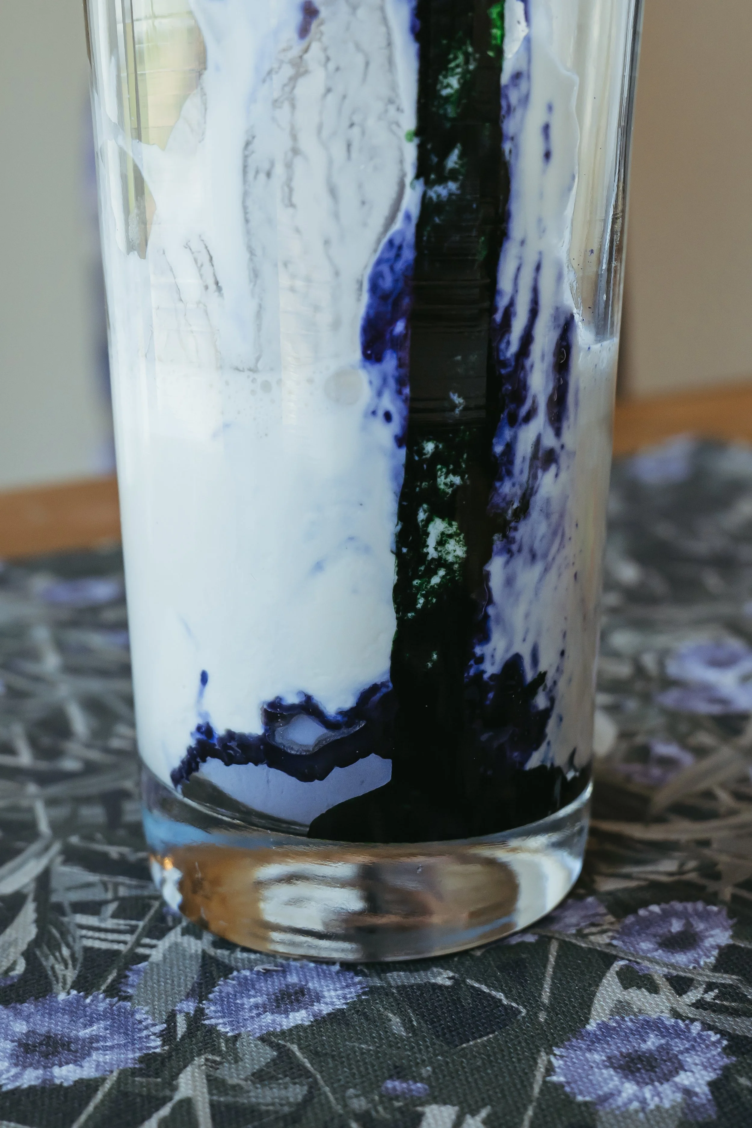 Close-up of a glass with dark blue and white ink swirling inside, creating an abstract pattern.