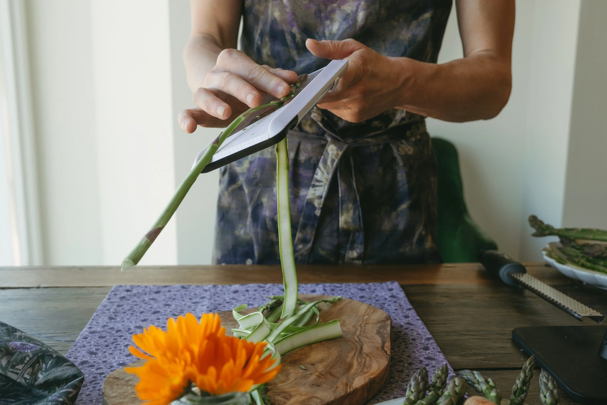Person preparing asparagus on a wooden cutting board in a kitchen, with orange marigold flowers nearby.