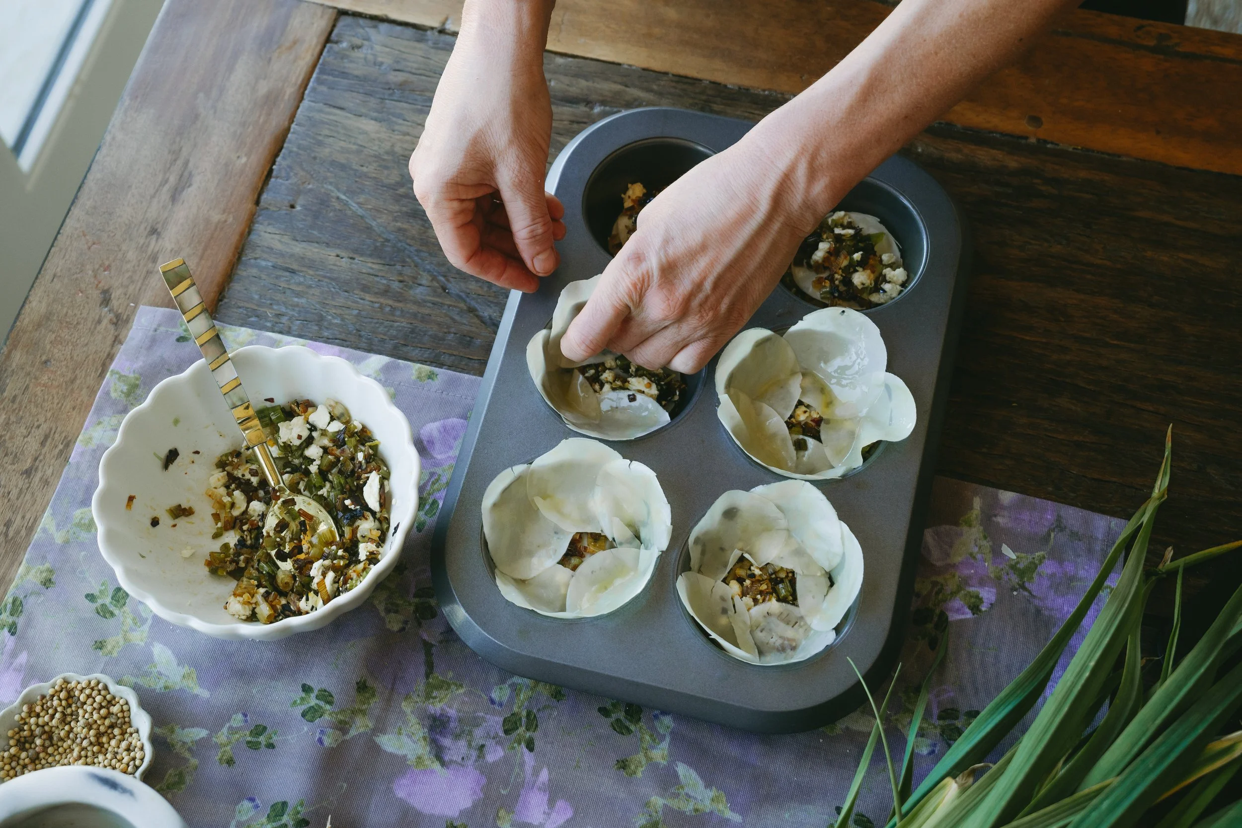 Hands preparing traditional dumplings with a filling of vegetables and cheese on a wooden table.