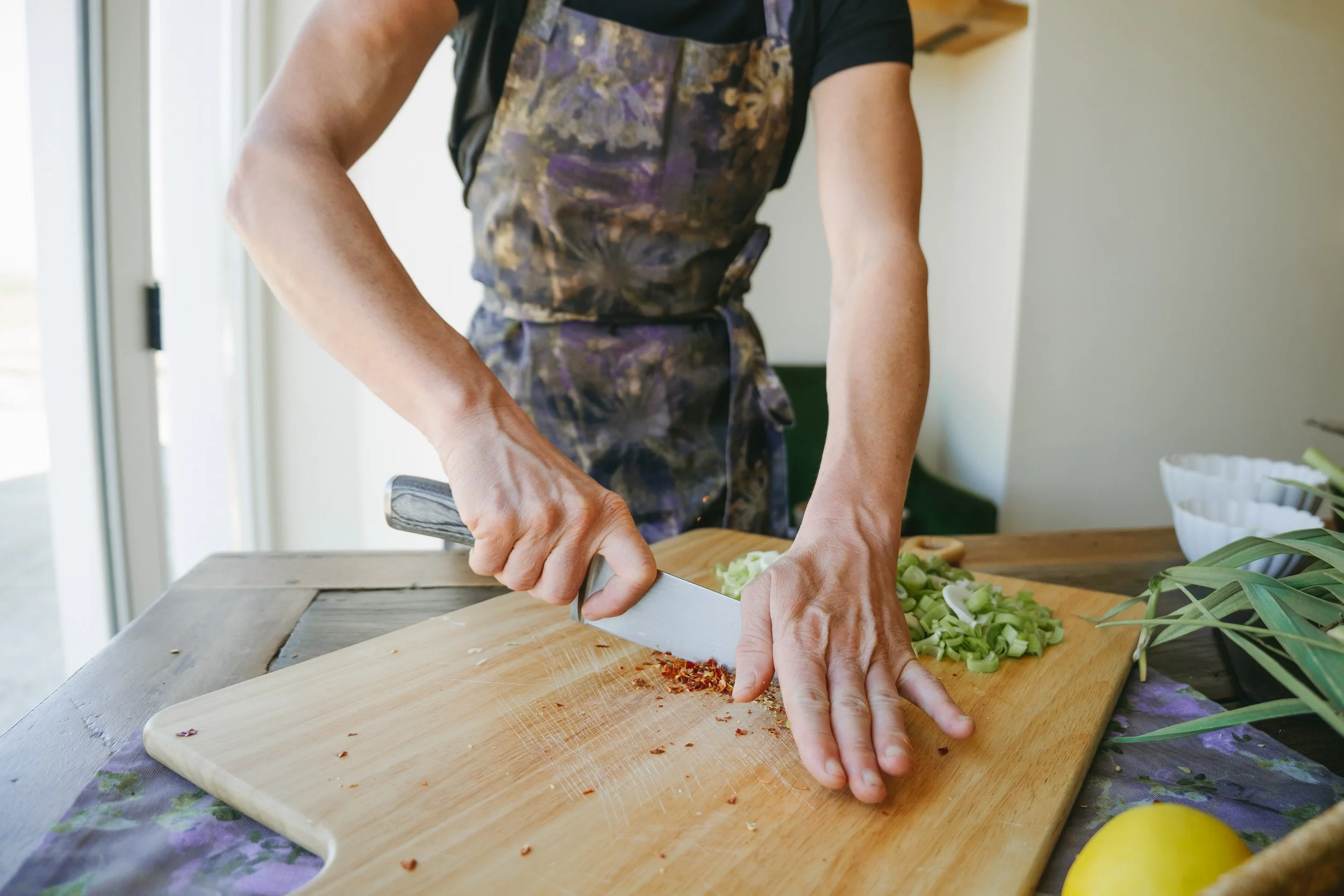 Person chopping vegetables on a wooden cutting board in a bright kitchen with natural light.