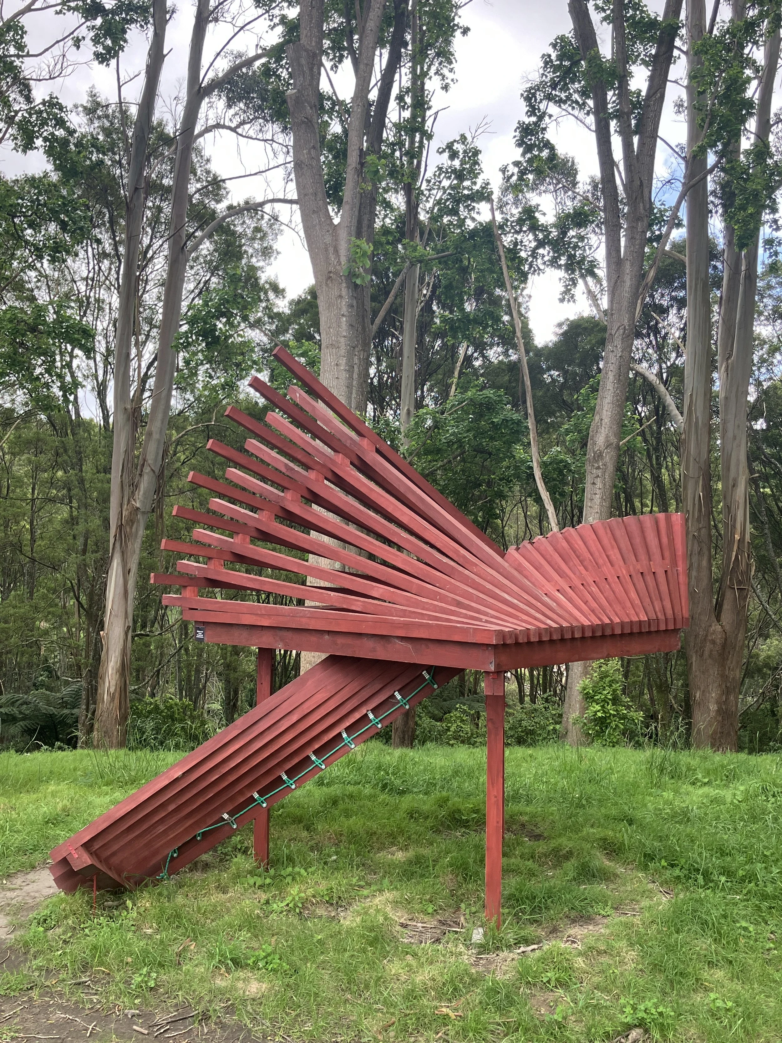 A red outdoor staircase with a curved railing leading up to a platform among trees in a forested area.
