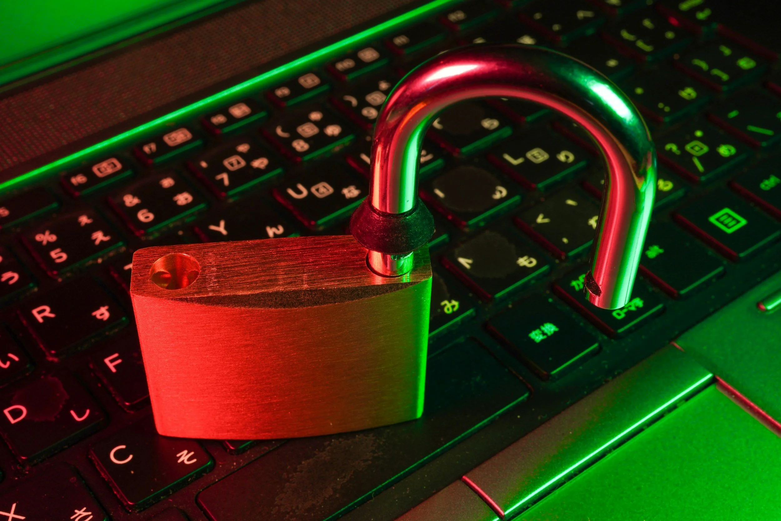 A red padlock with an open shackle placed on a backlit keyboard with green and red lighting effects.