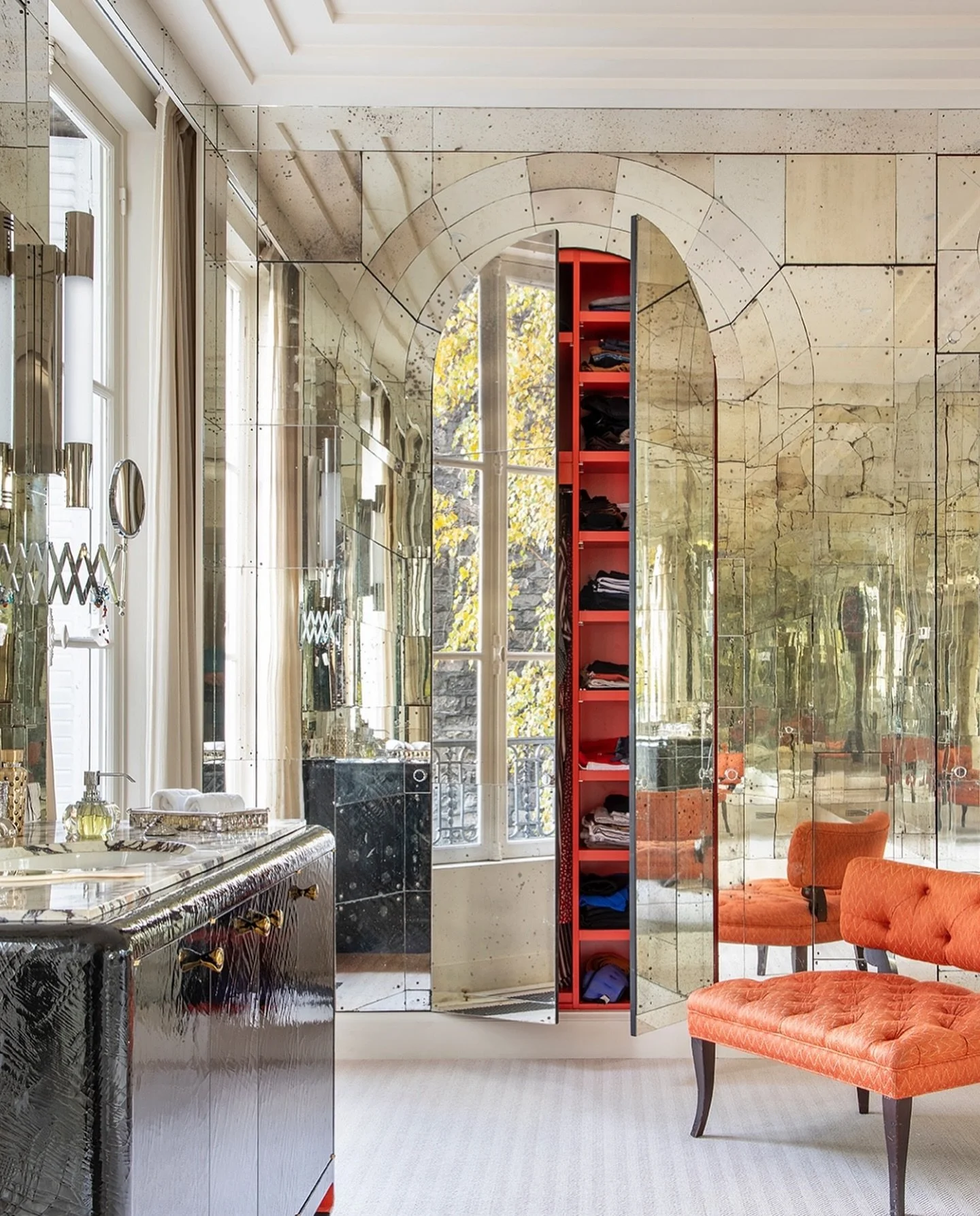 A master bathroom that plays with illusions, designed by Pinto. Vintage 1940s engraved mirrors form a stunning trellis effect, concealing a striking red dressing room. The endless reflections and intricate details turn this functional space into a re