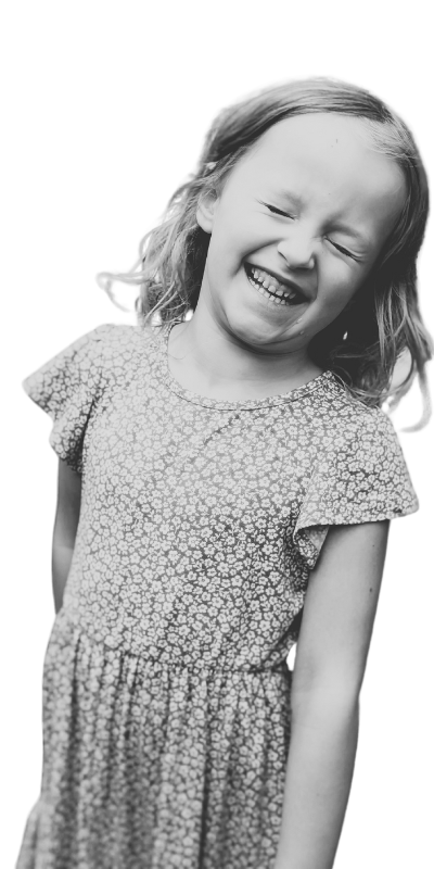 A young girl with light hair and a patterned dress, smiling and laughing with eyes closed.