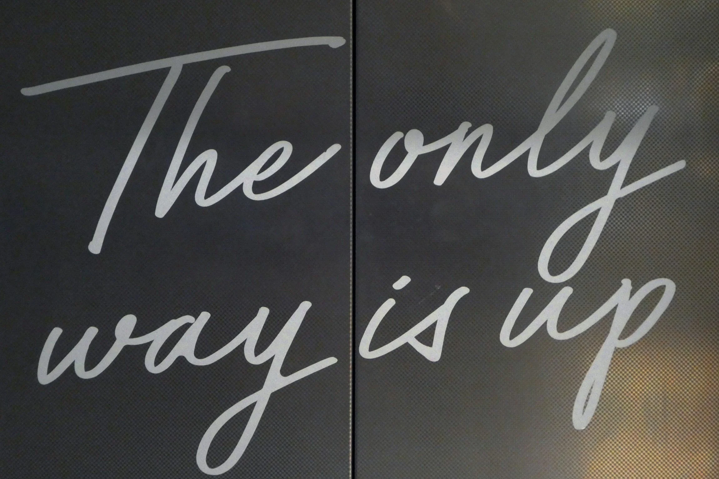 Sign with the phrase 'The only way is up' written in white cursive letters on a black background.